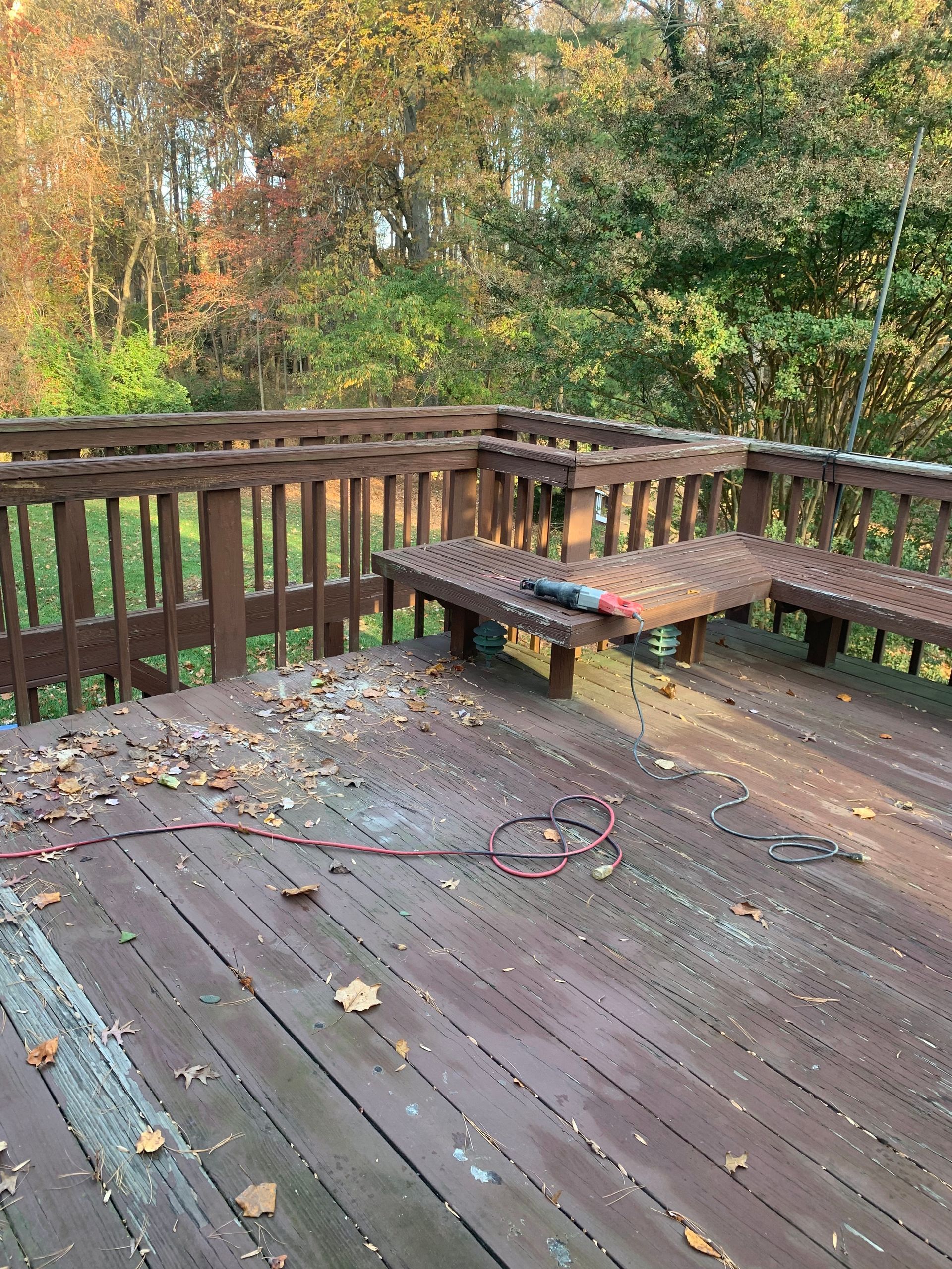 Wooden deck with built-in benches, brown railing, fallen leaves, and wooded background.