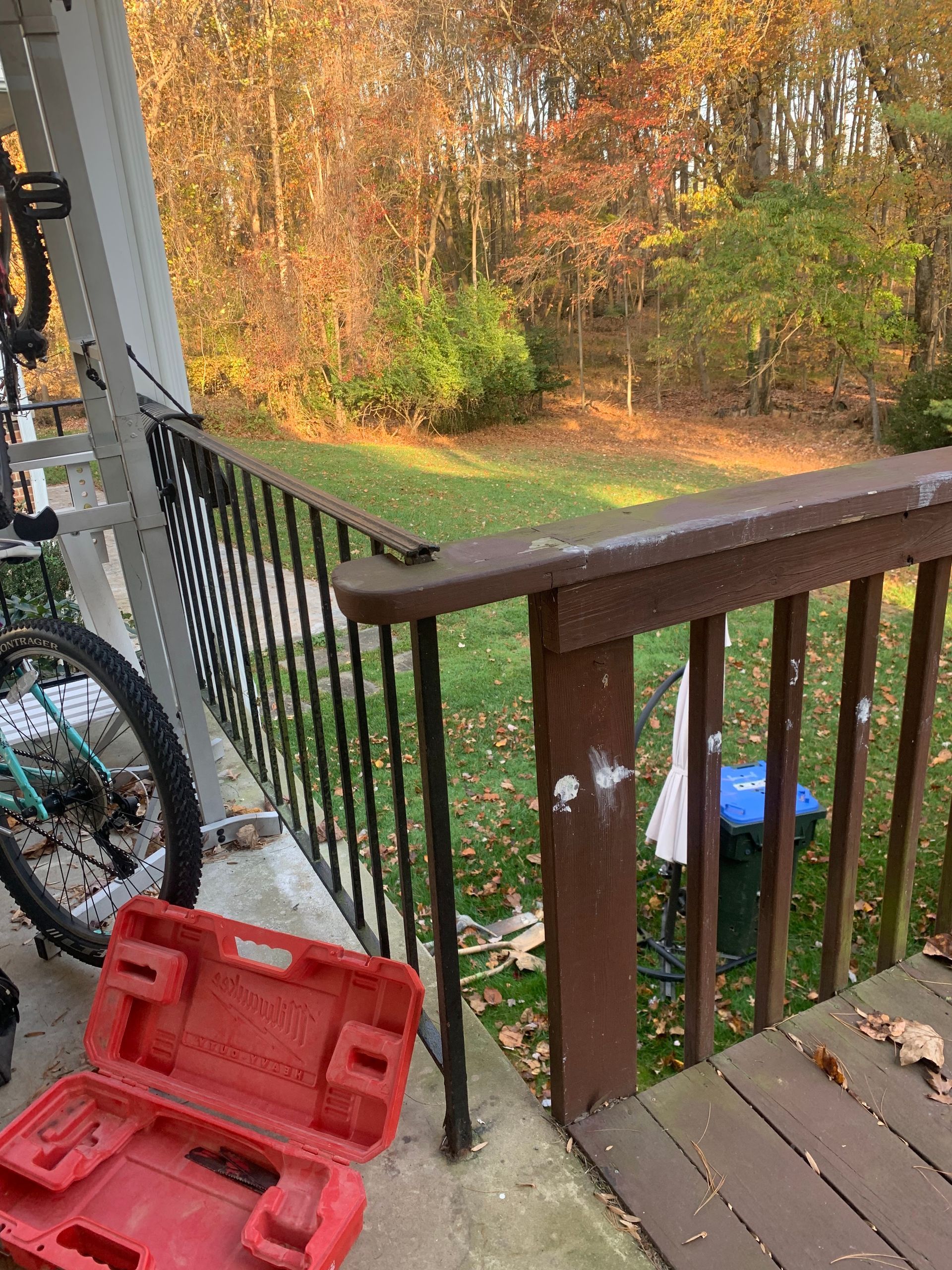 Red toolbox and bicycle on porch, overlooking a yard with autumn foliage.