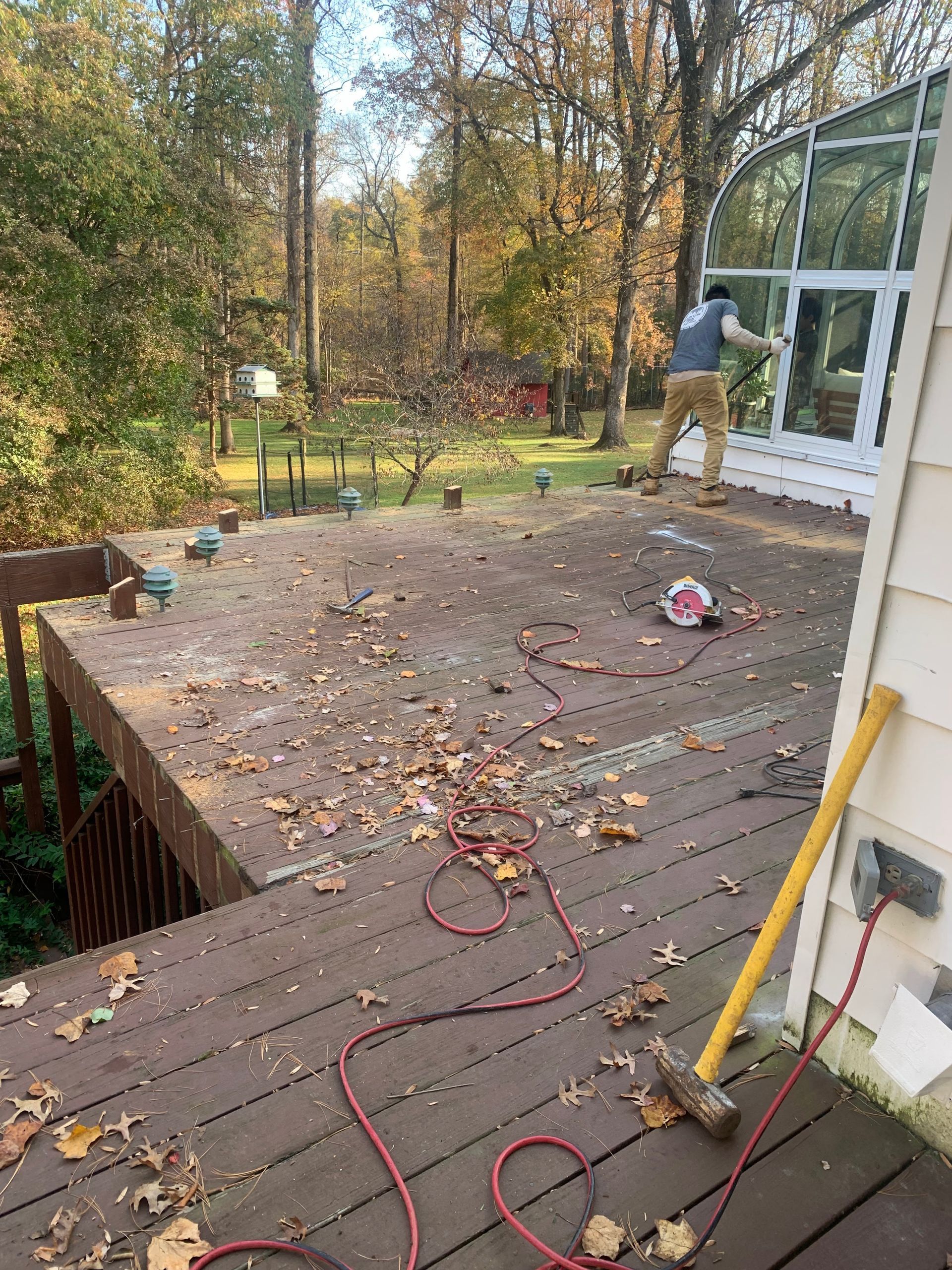 Person working on a deck, with tools and leaves scattered. Trees in the background.