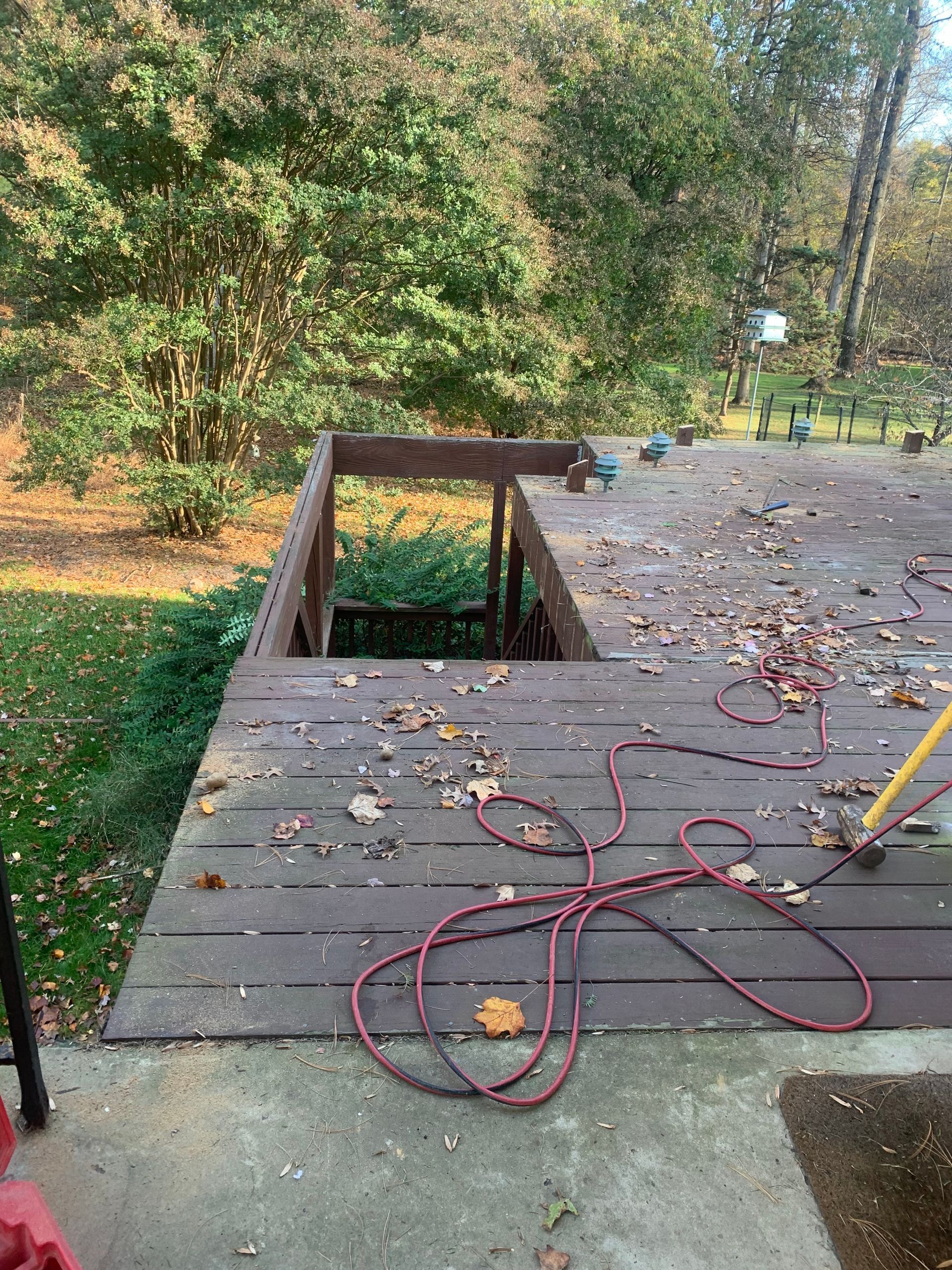Deck with missing section, leaves, and red hose, surrounded by trees.