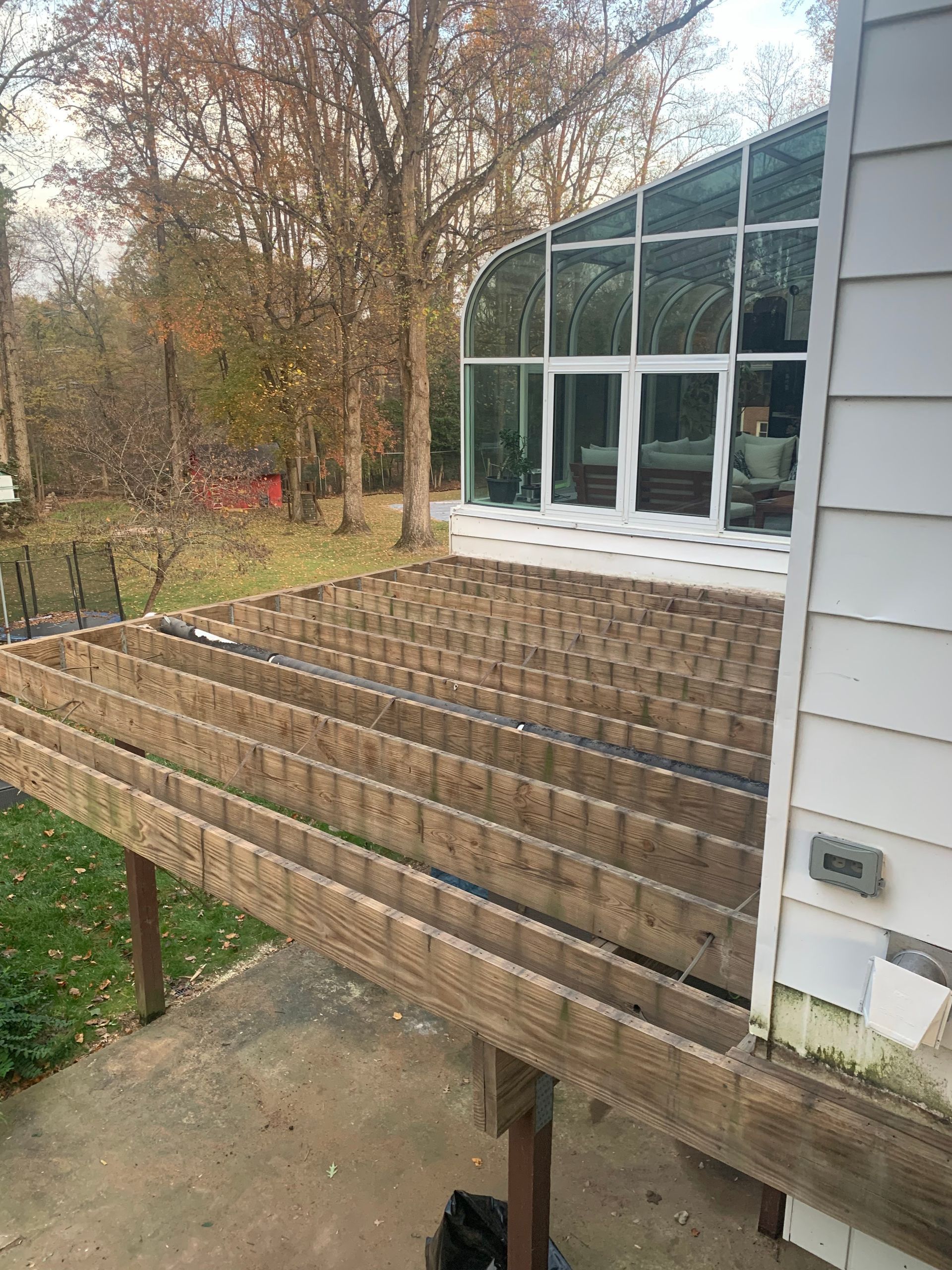 Deck under construction, with exposed wooden beams, next to a sunroom and siding of a house.