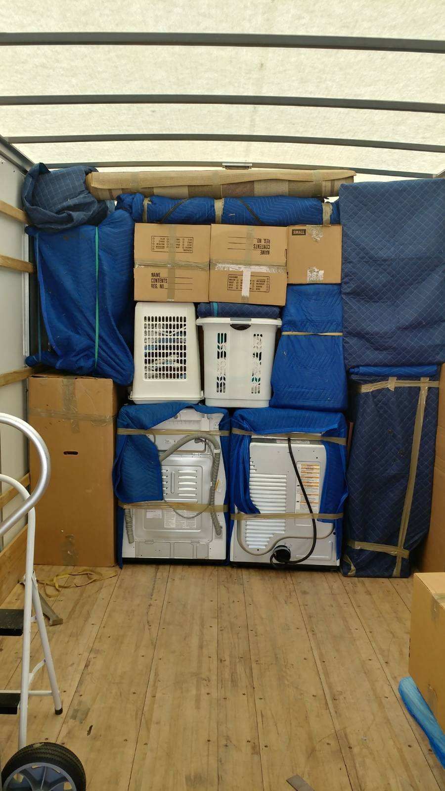 Interior view of a moving truck loaded with household items; boxes, wrapped appliances, and furniture.