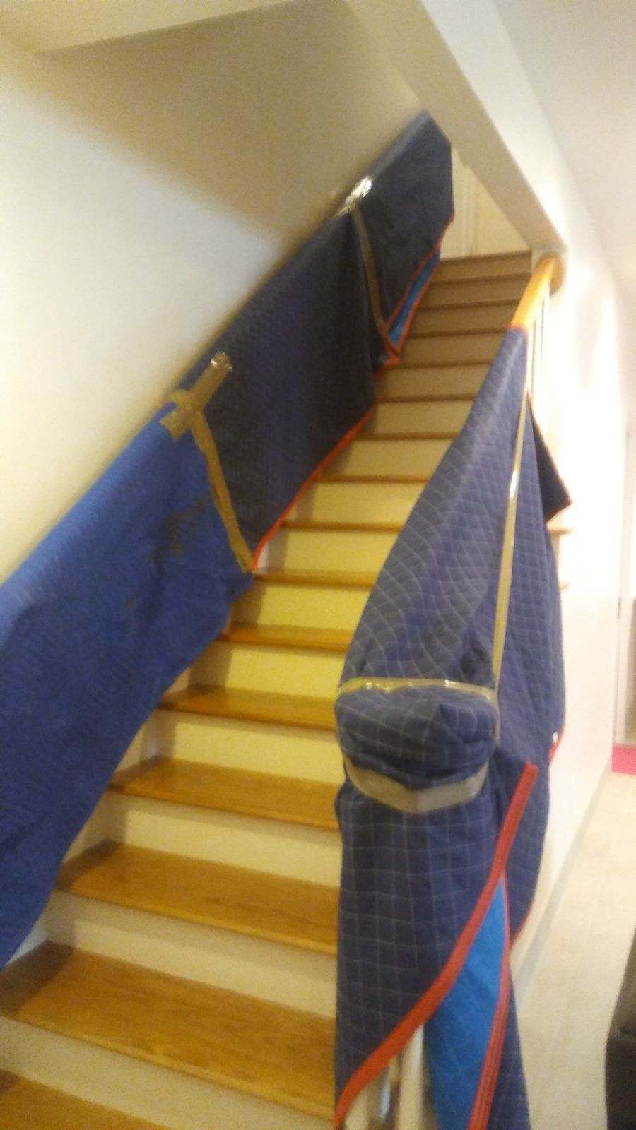 Staircase covered with blue moving blankets to protect it during furniture transport, showing wooden stairs and white walls.