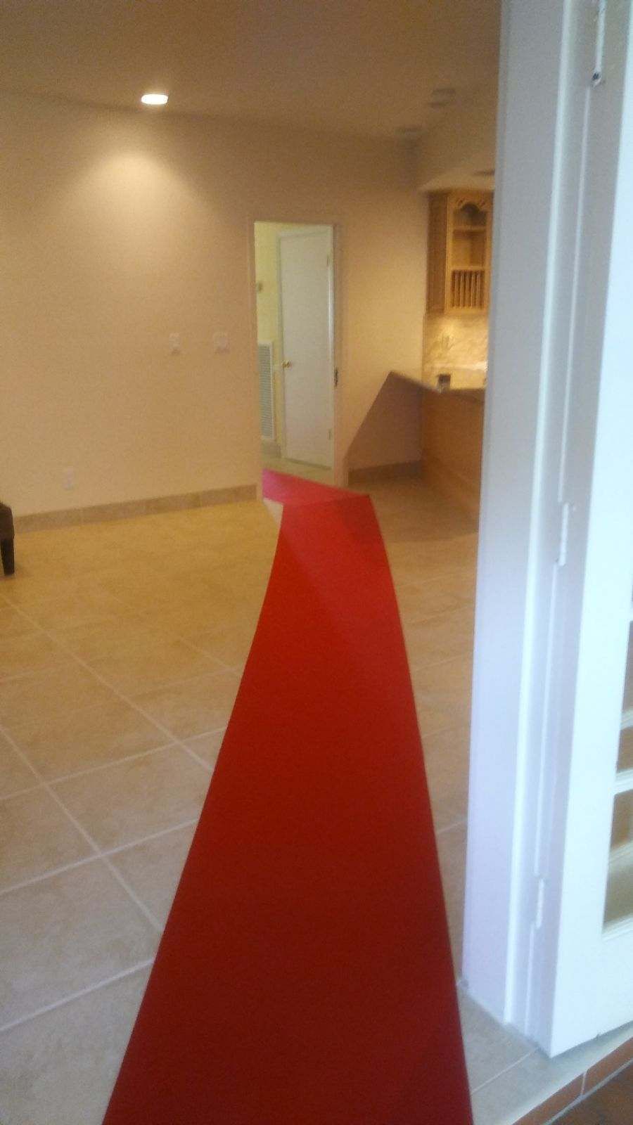 A long red carpet leads down a tiled hallway towards a door and a kitchen area.