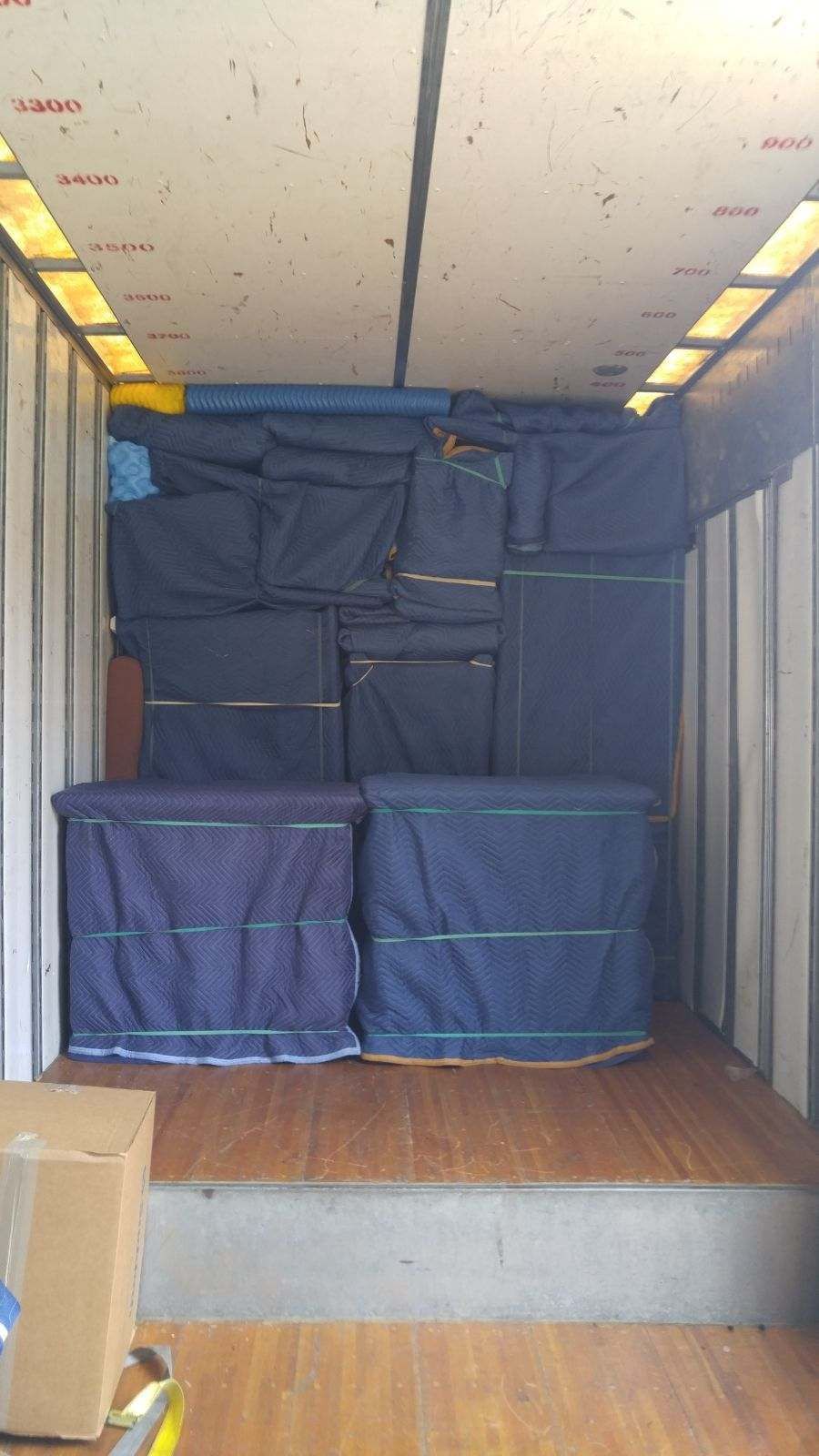 Interior of a moving truck filled with furniture wrapped in blue moving blankets and boxes.