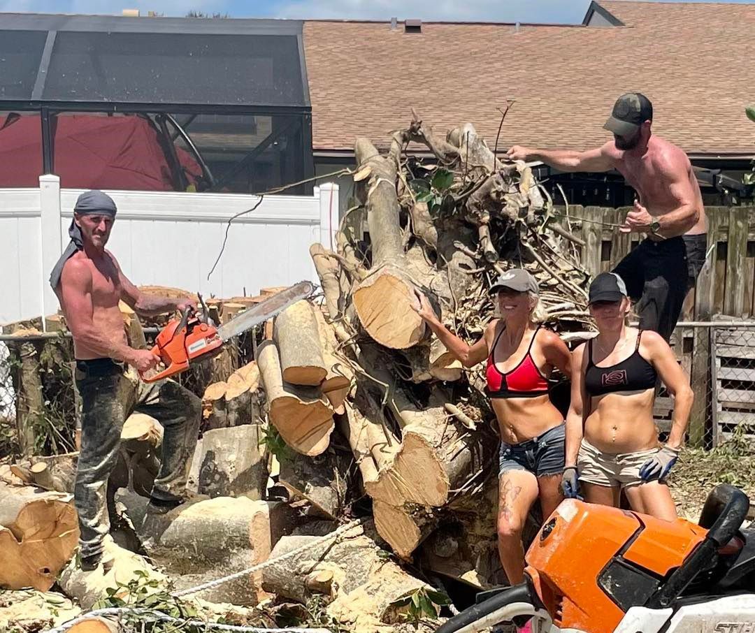 A group of people are standing around a pile of logs.