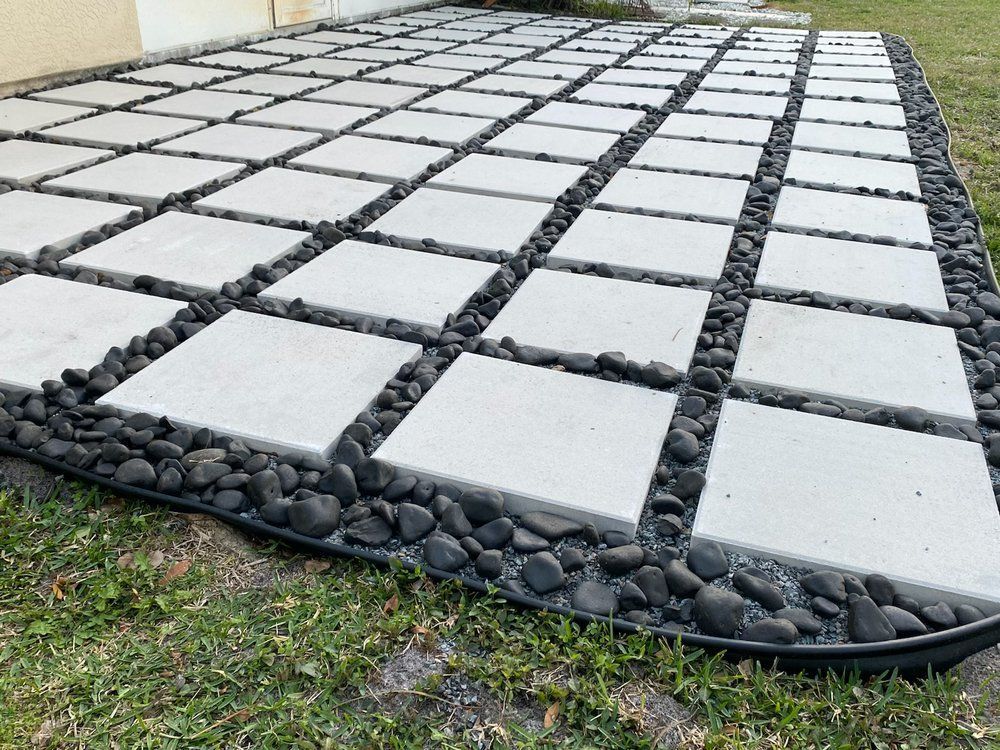A patio with square tiles and black rocks surrounding it