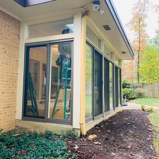 A man is standing on a ladder in front of a house with sliding glass doors.
