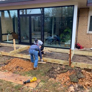 Two men are working on a wooden deck in front of a house.