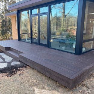 A wooden deck is in front of a house with lots of windows.