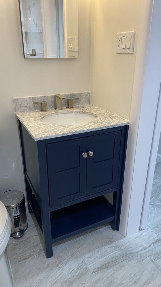 A bathroom with a blue vanity , sink , mirror and trash can.
