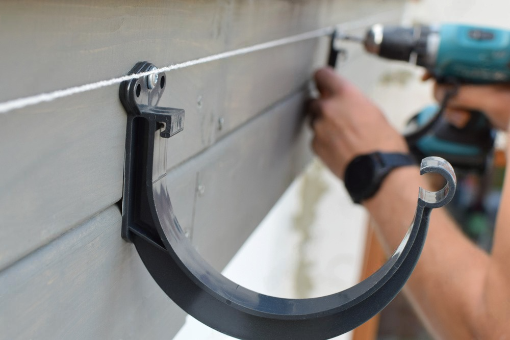 A man is installing a gutter hook with a drill.