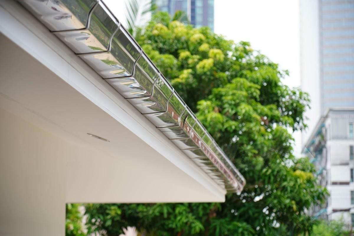 A gutter on the side of a building with trees in the background.