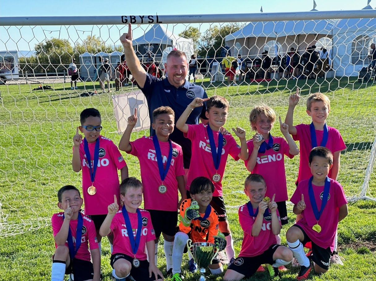 A group of young boys are posing for a picture on a soccer field having won championship.