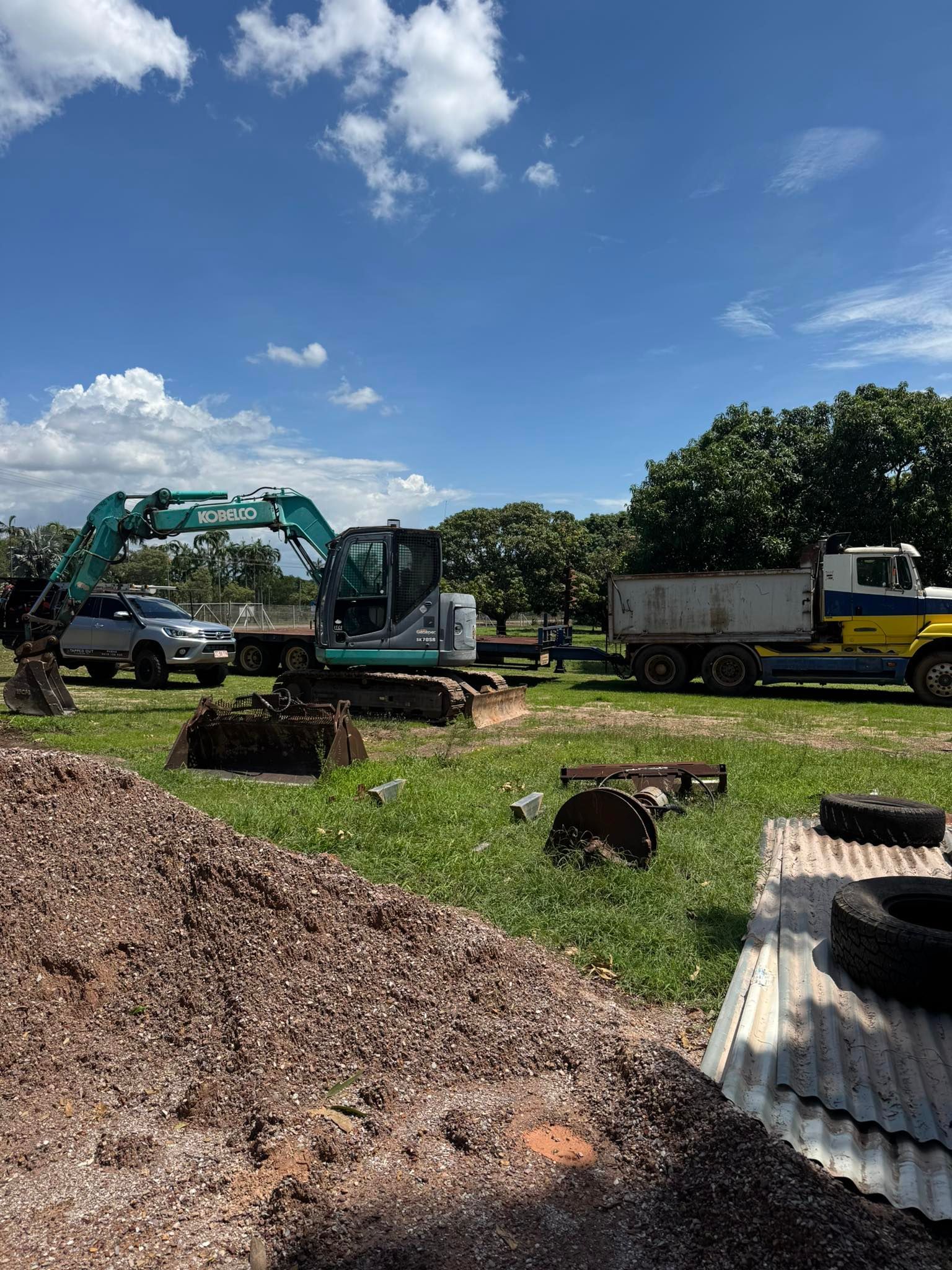 An Excavator Loading a Dump Truck in a Grassy Field with a Blue Sky — Tapped Out Plumbing NT in Bellamack, NT