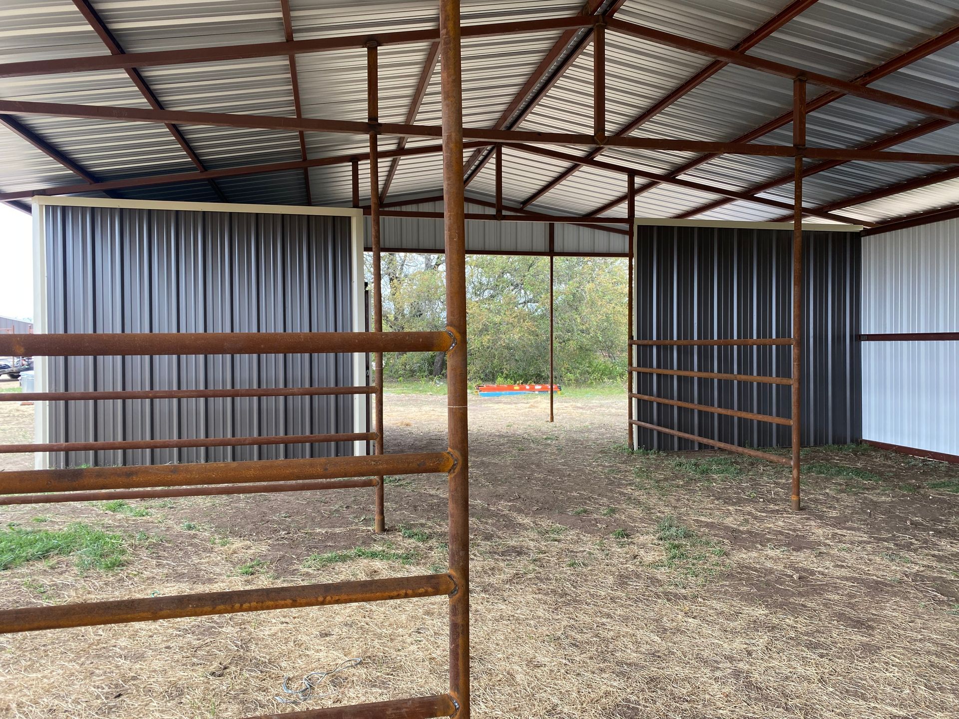 An empty barn with a metal roof and a wooden fence.