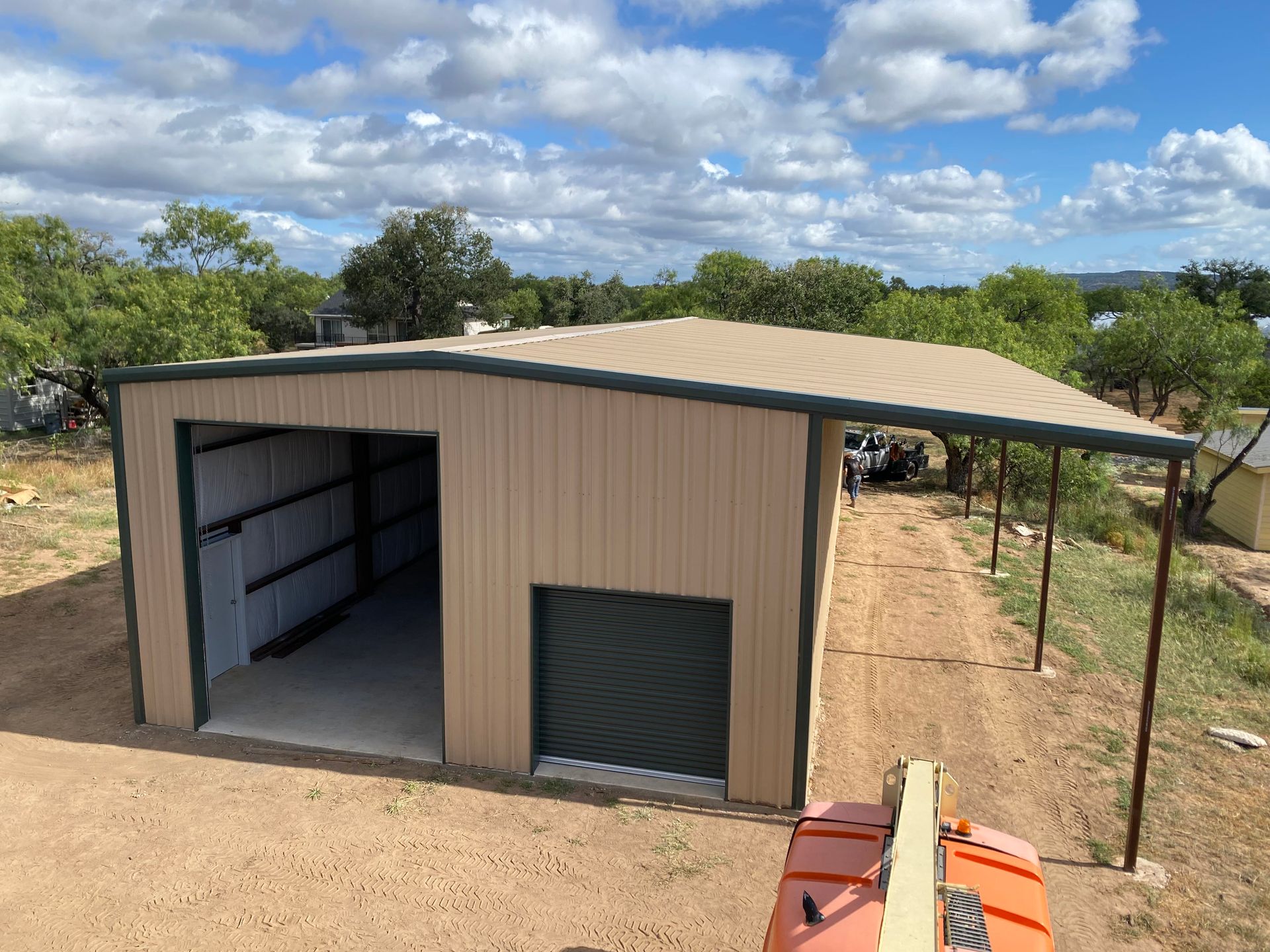 An aerial view of a metal building with a carport and trees in the background.