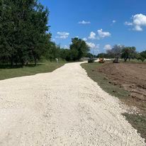 A dirt road going through a field with trees on both sides.