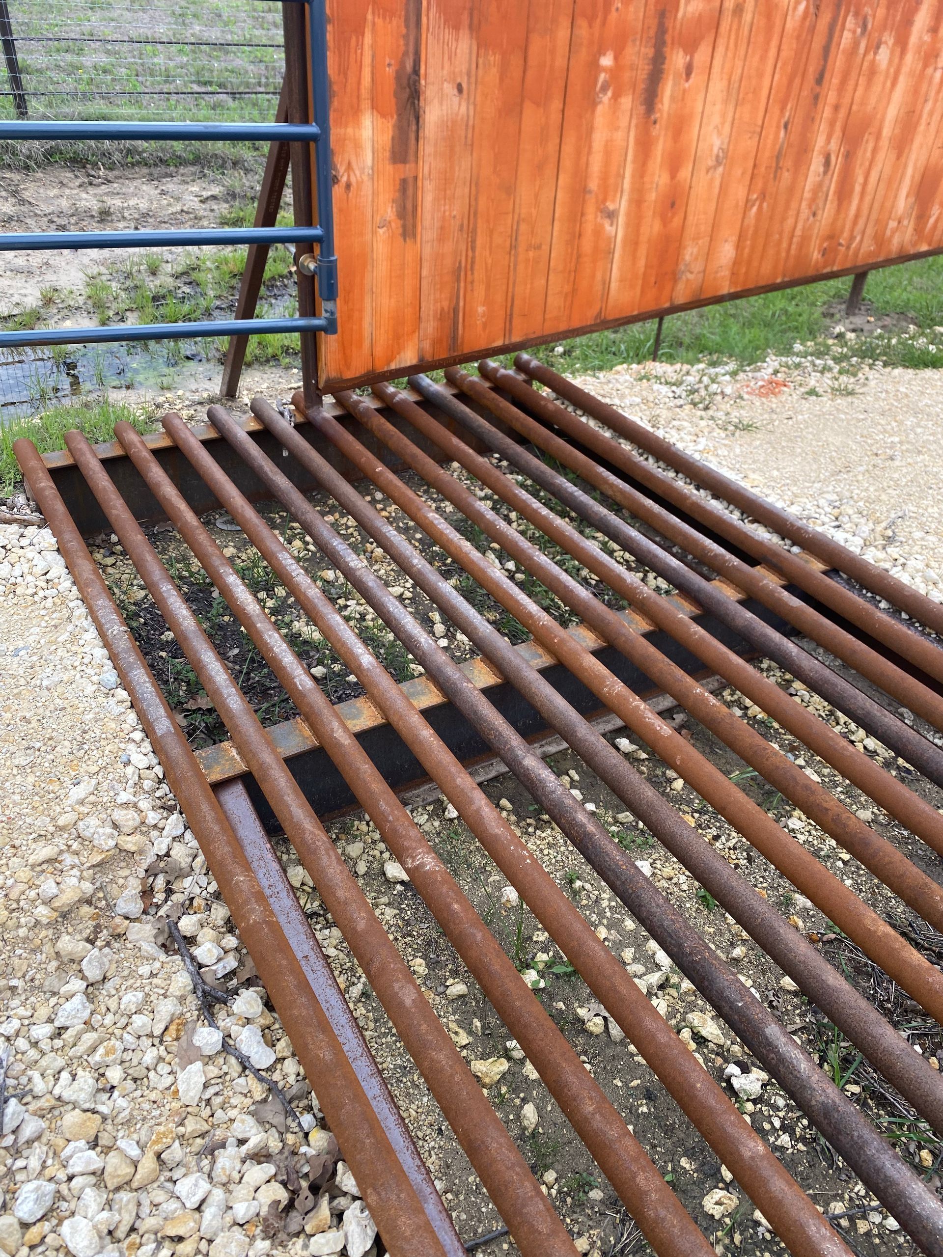 A rusty metal fence with a wooden fence in the background