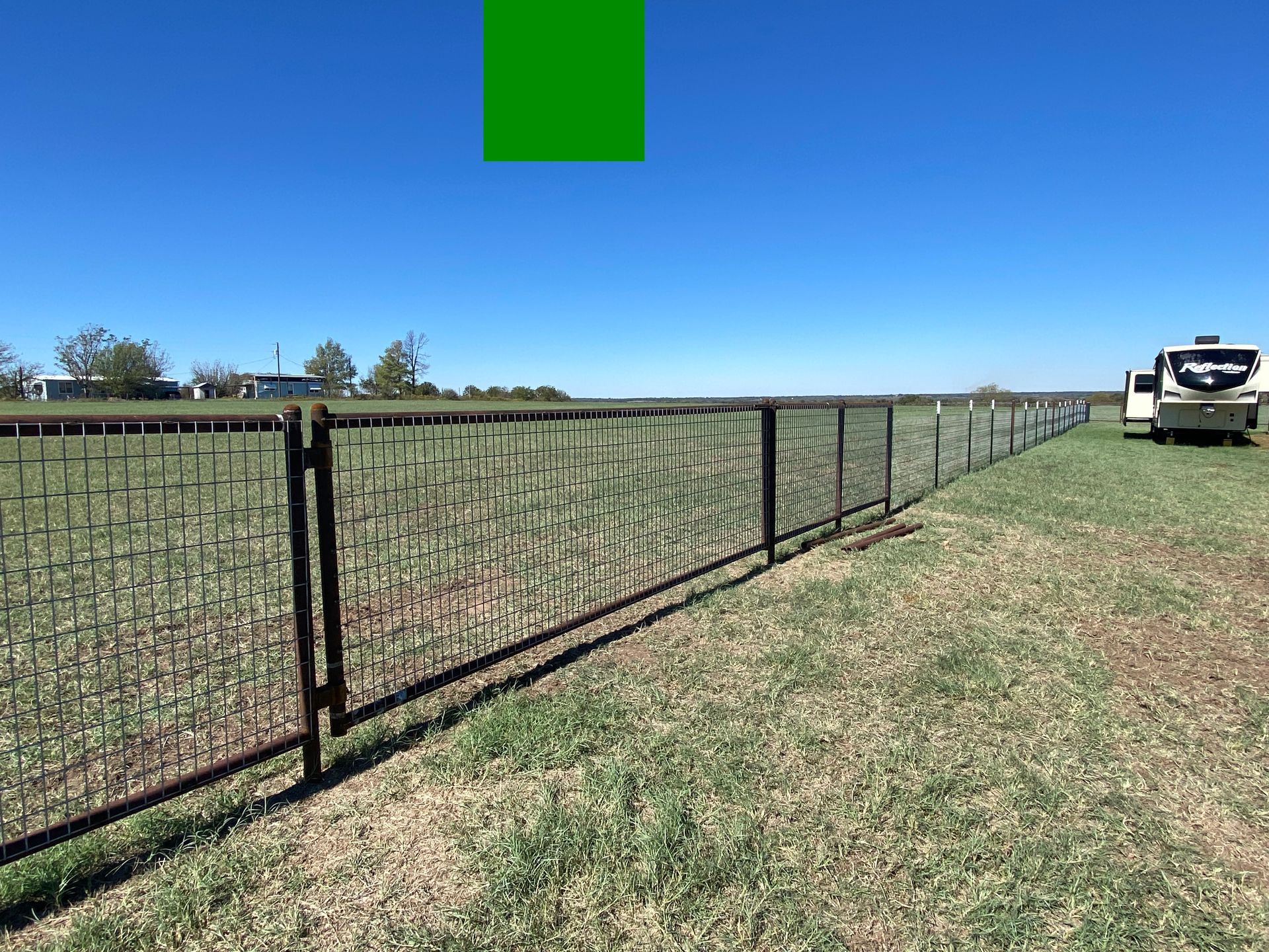 A fence surrounds a grassy field with a truck parked in the background.