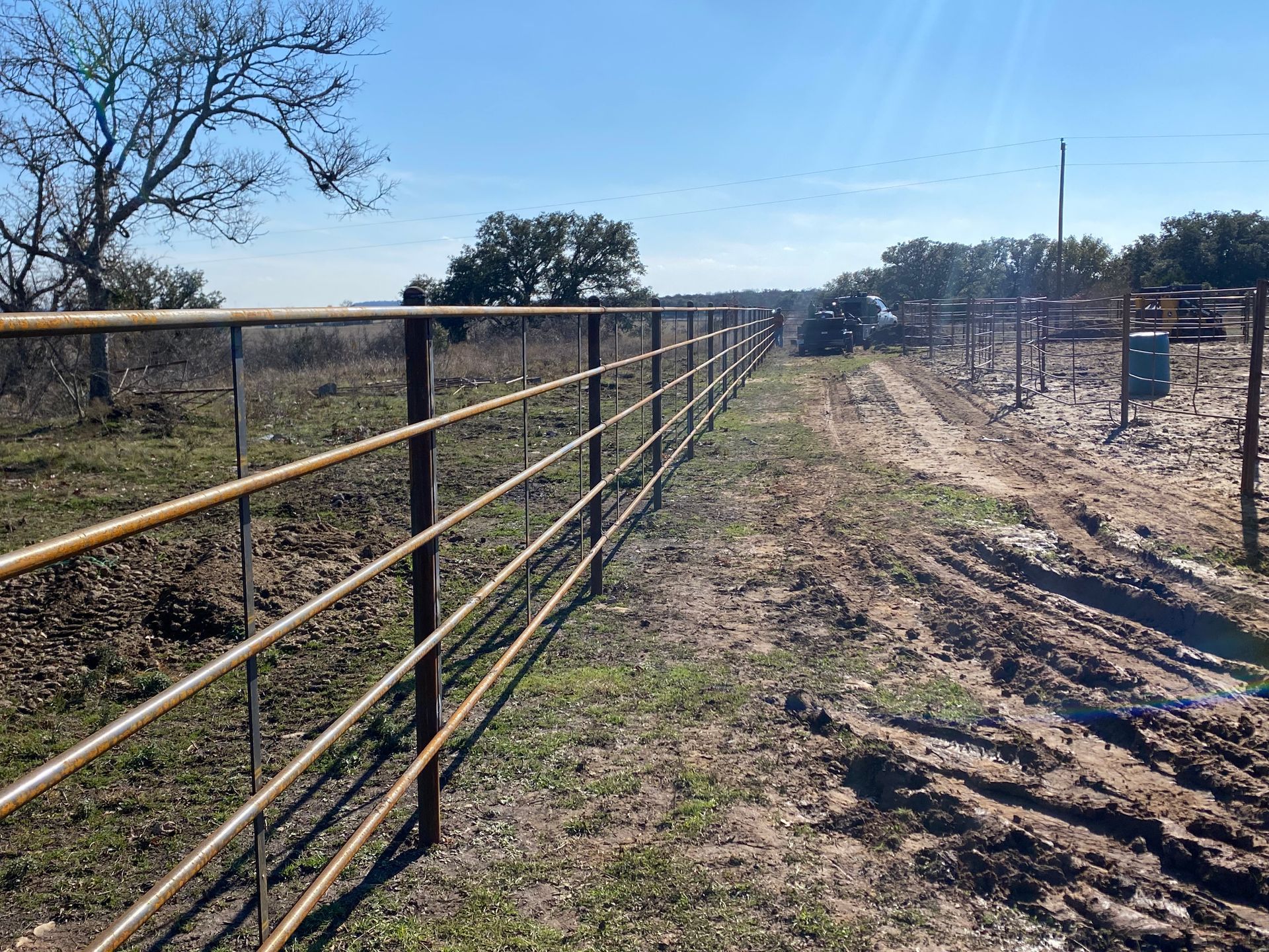 A long metal fence surrounds a dirt road in a field.
