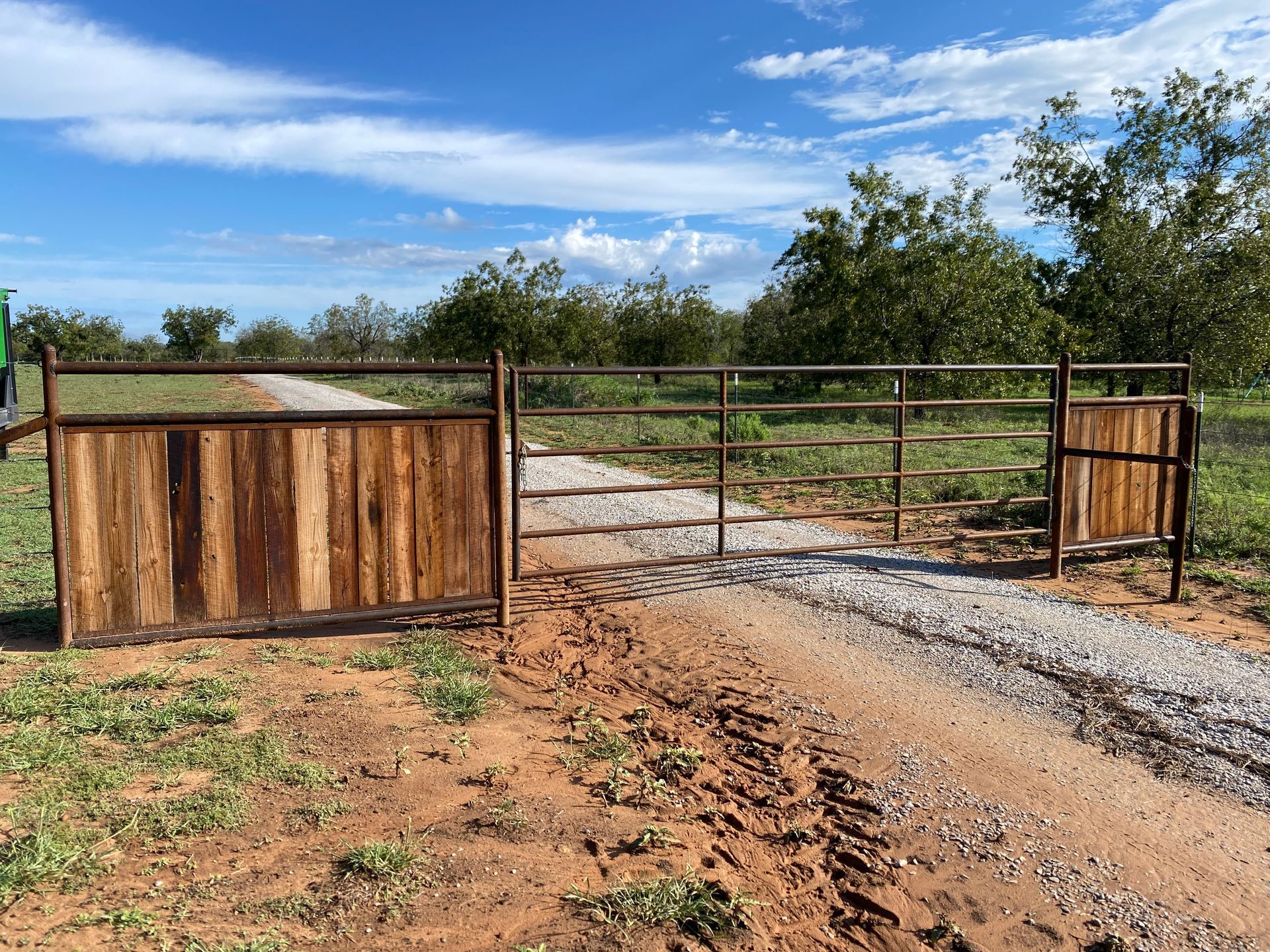 A wooden gate is sitting on the side of a dirt road.