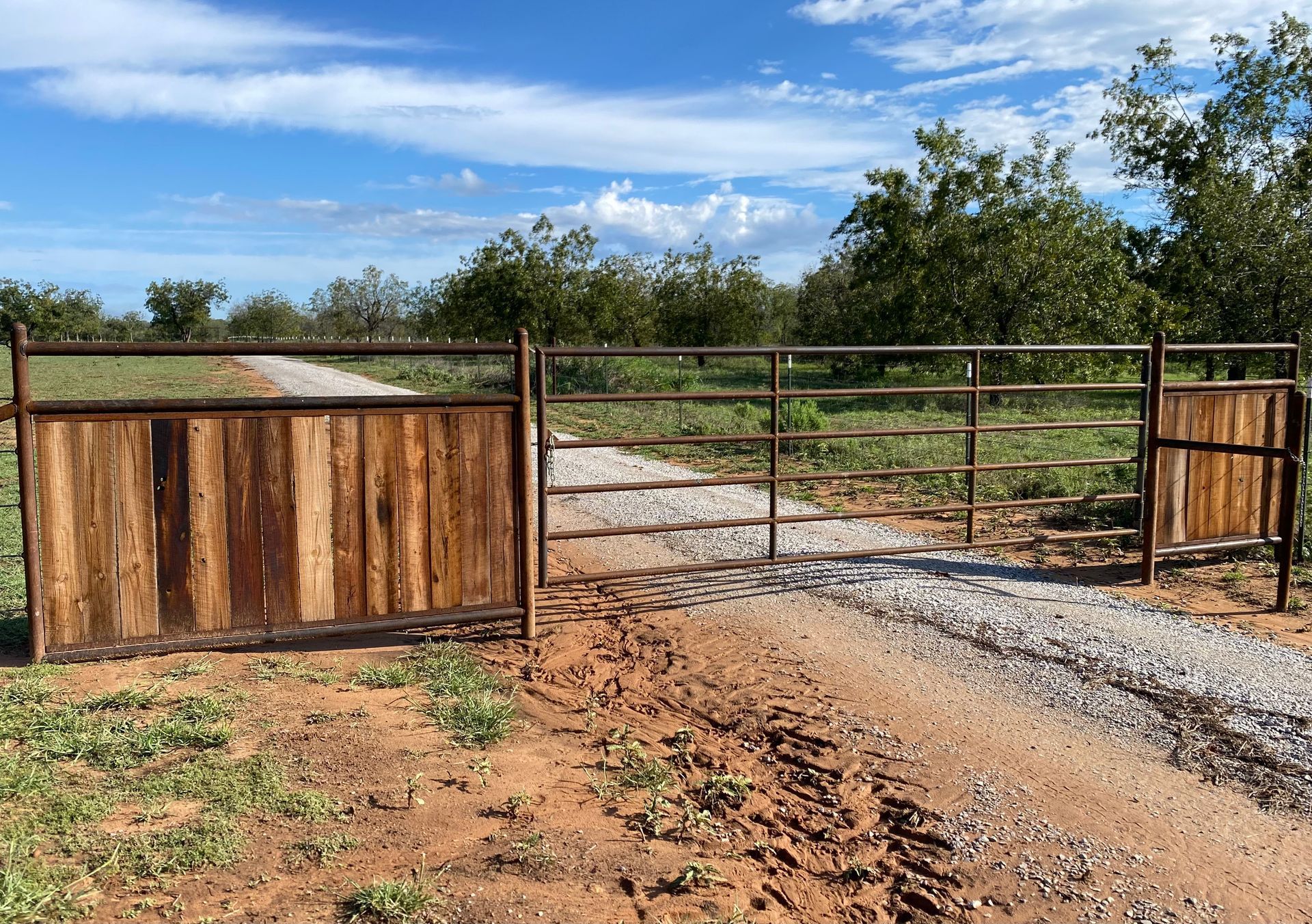 A wooden gate is sitting on the side of a dirt road.