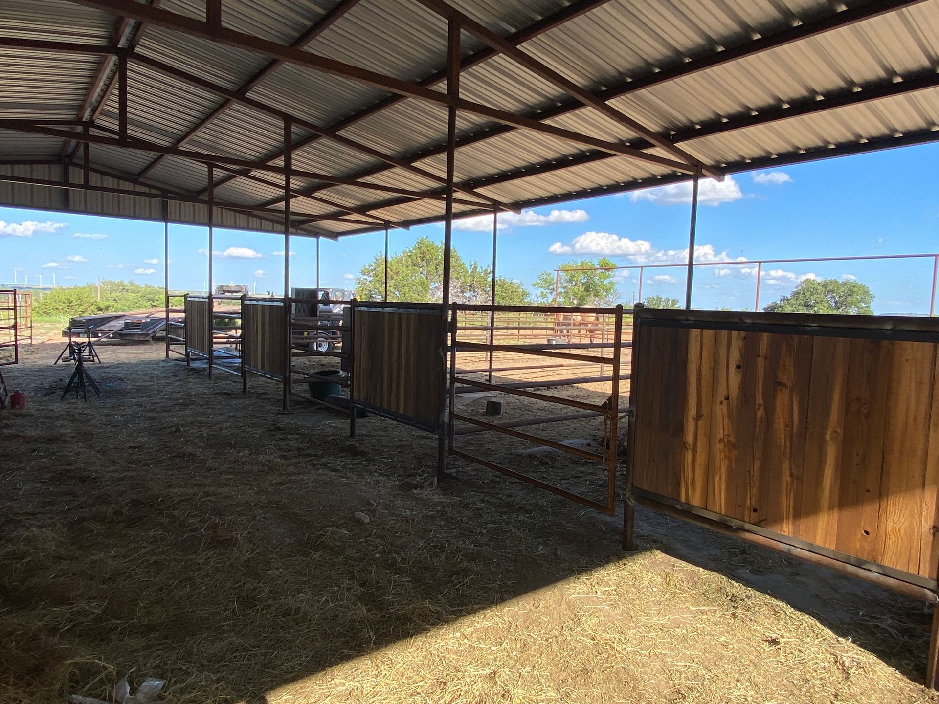 A horse stable with a metal roof and wooden fences filled with hay.