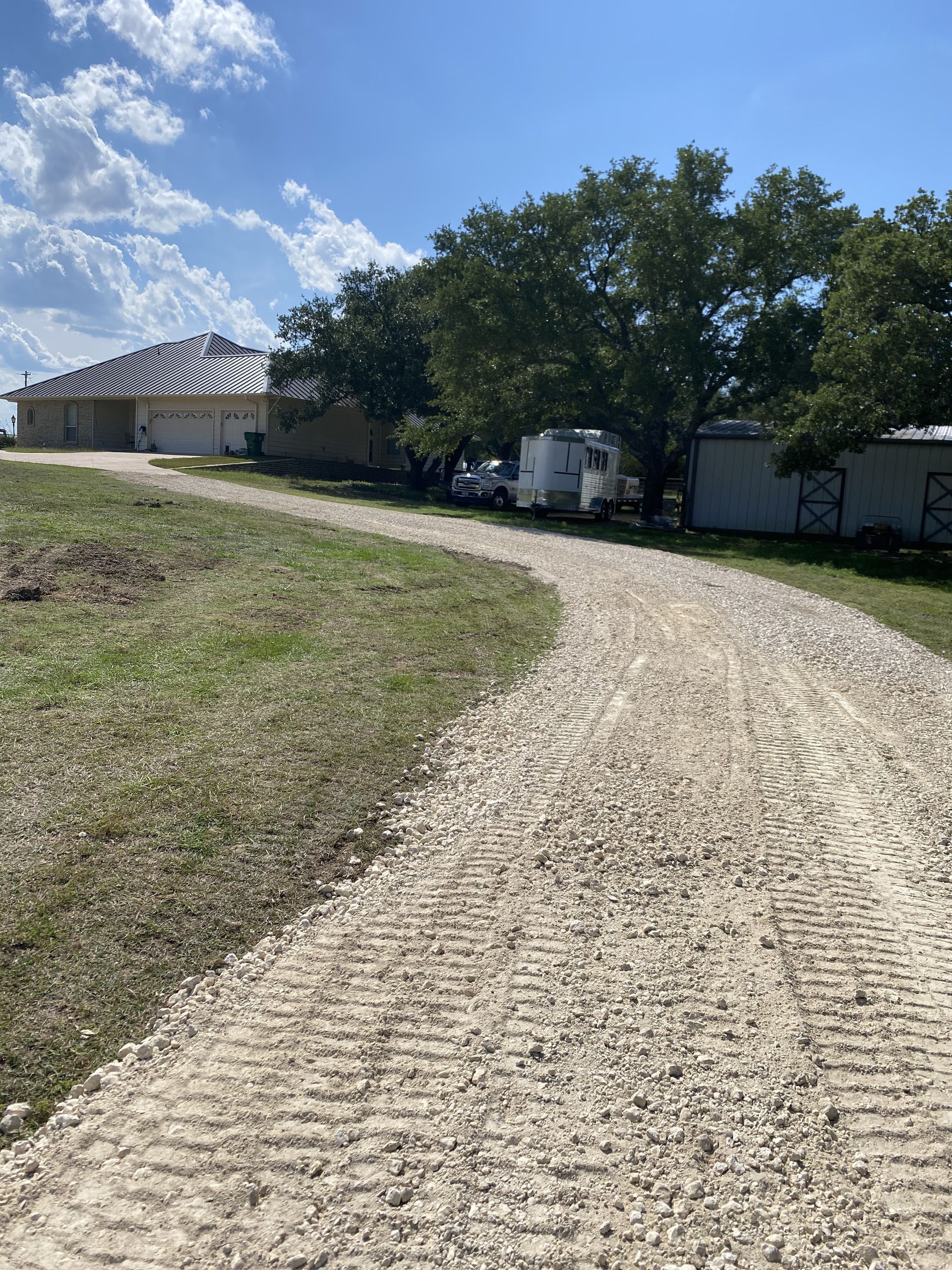 A dirt road leading to a house with a trailer parked on the side of it.