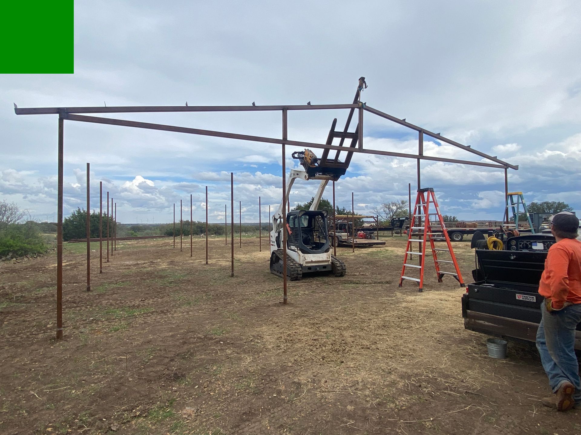 A man is standing in a field next to a ladder and a bulldozer.