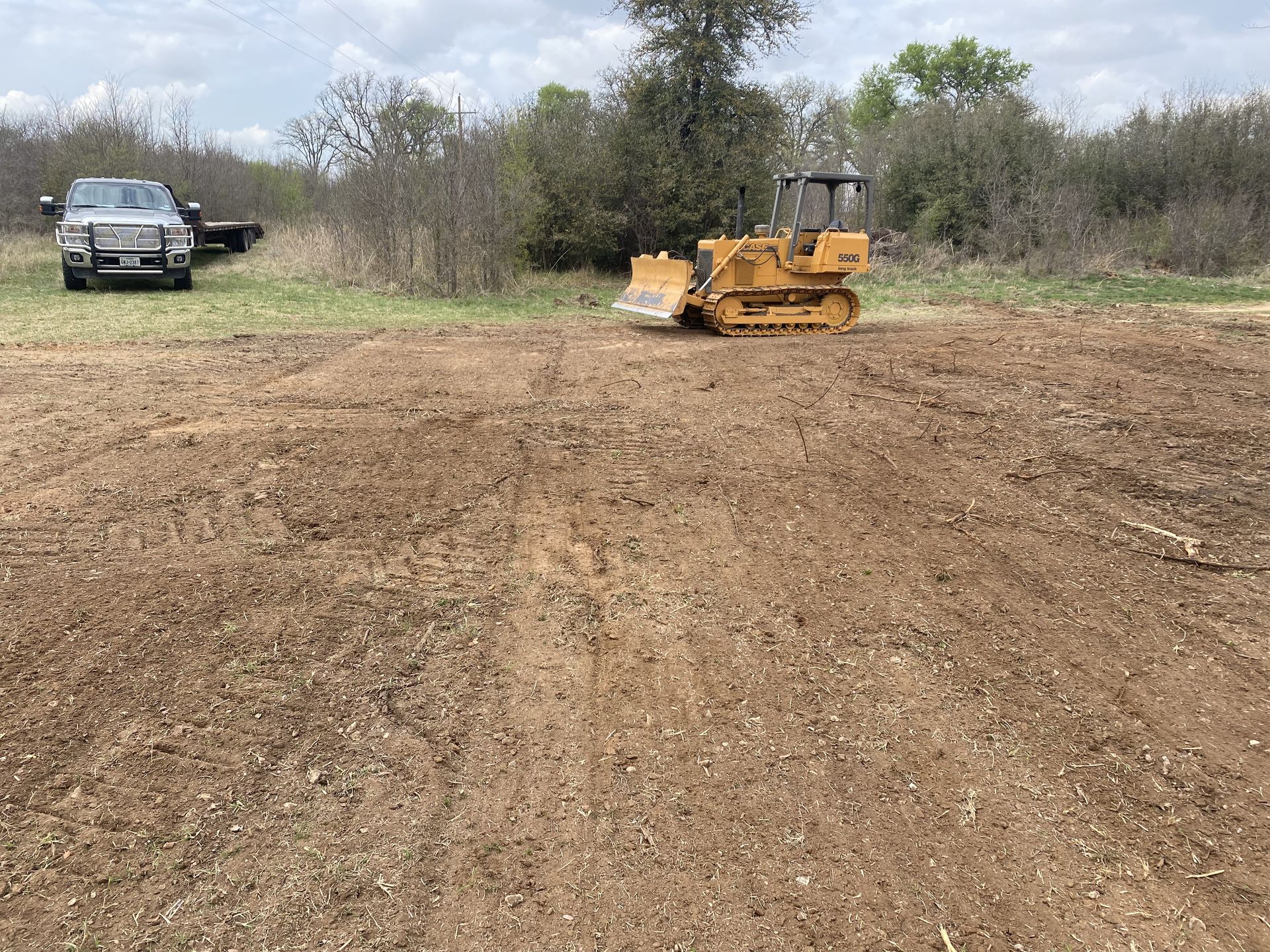 A bulldozer is moving dirt in a field next to a truck.