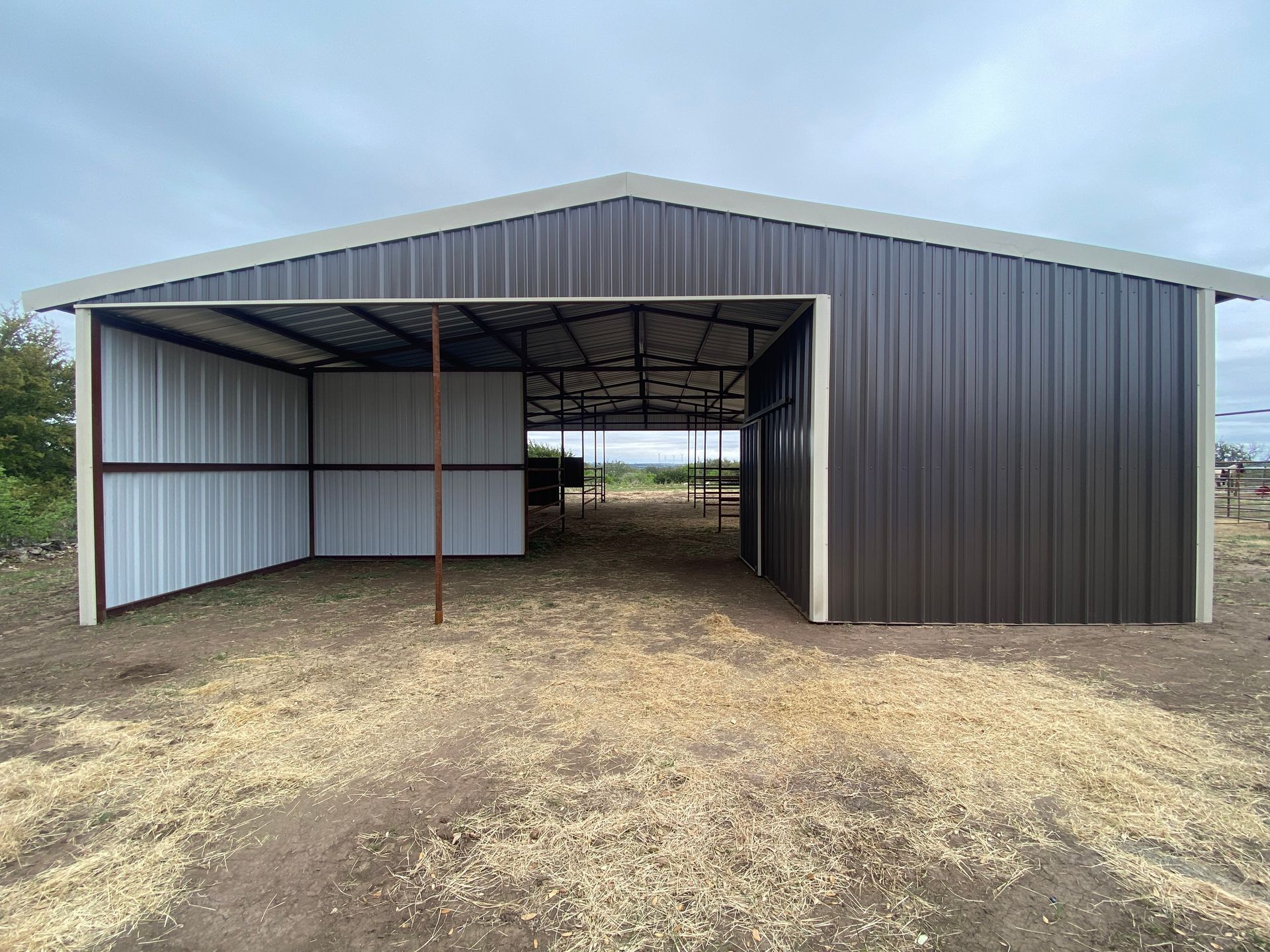 A large metal barn is sitting in the middle of a dirt field.