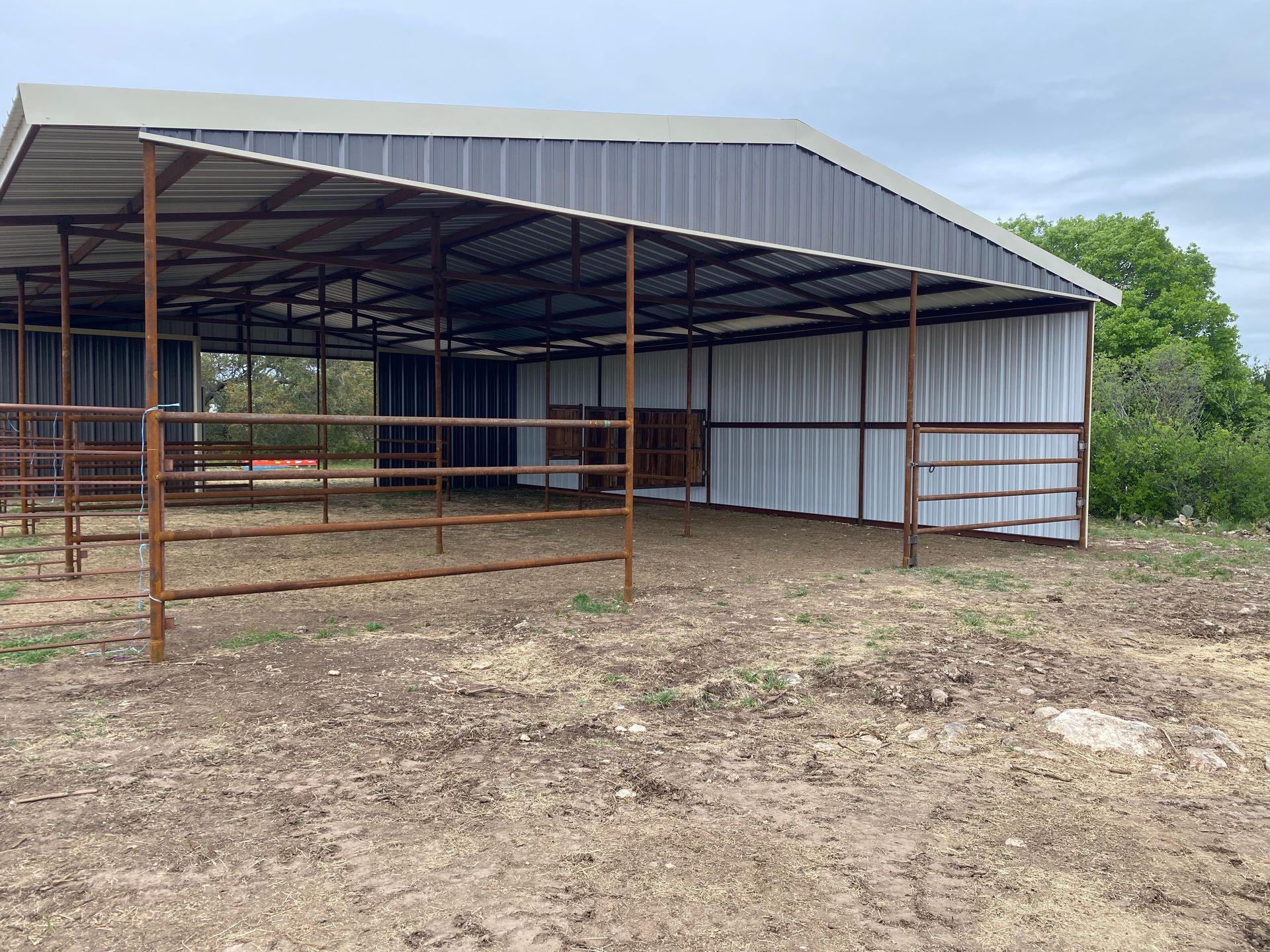 A large metal barn with a fence around it is sitting in the middle of a dirt field.