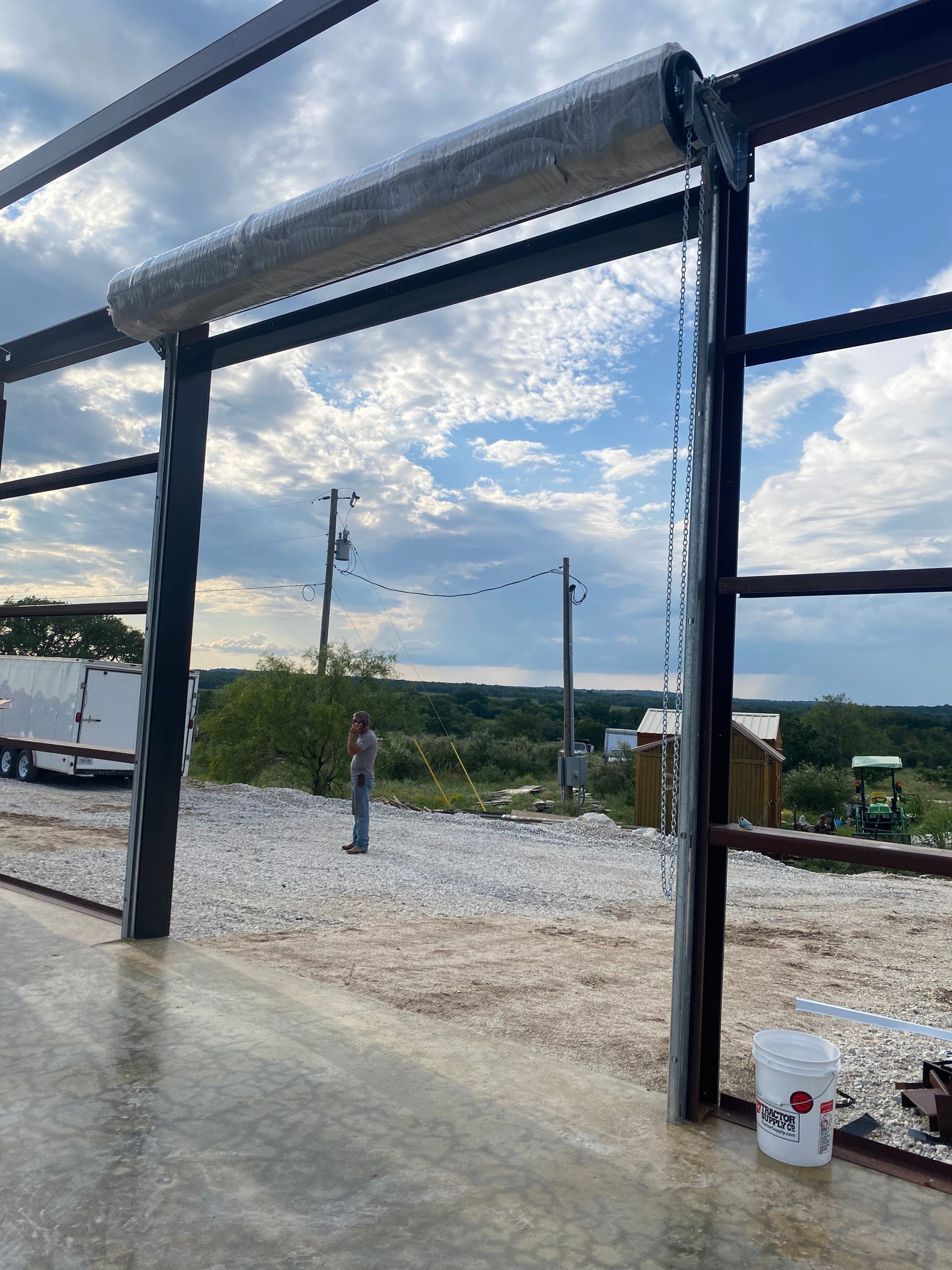 A man is standing in front of a fence with a bucket next to it.