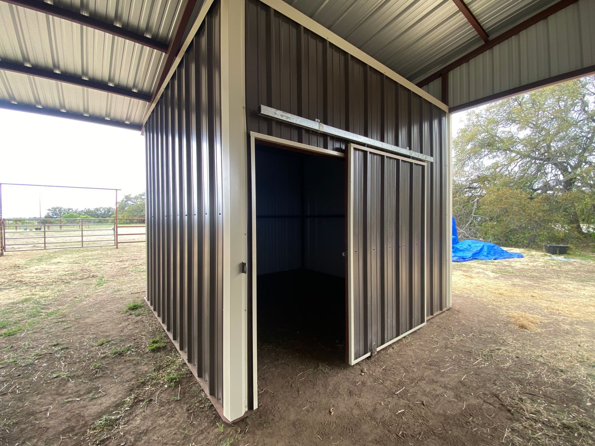 A shed with a sliding door is sitting in the middle of a dirt field.