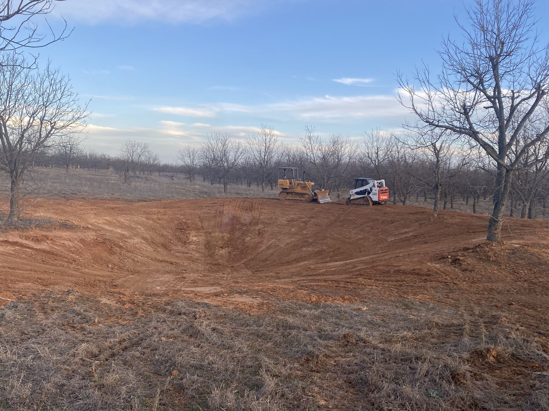 A bulldozer is moving dirt in a field with trees in the background.