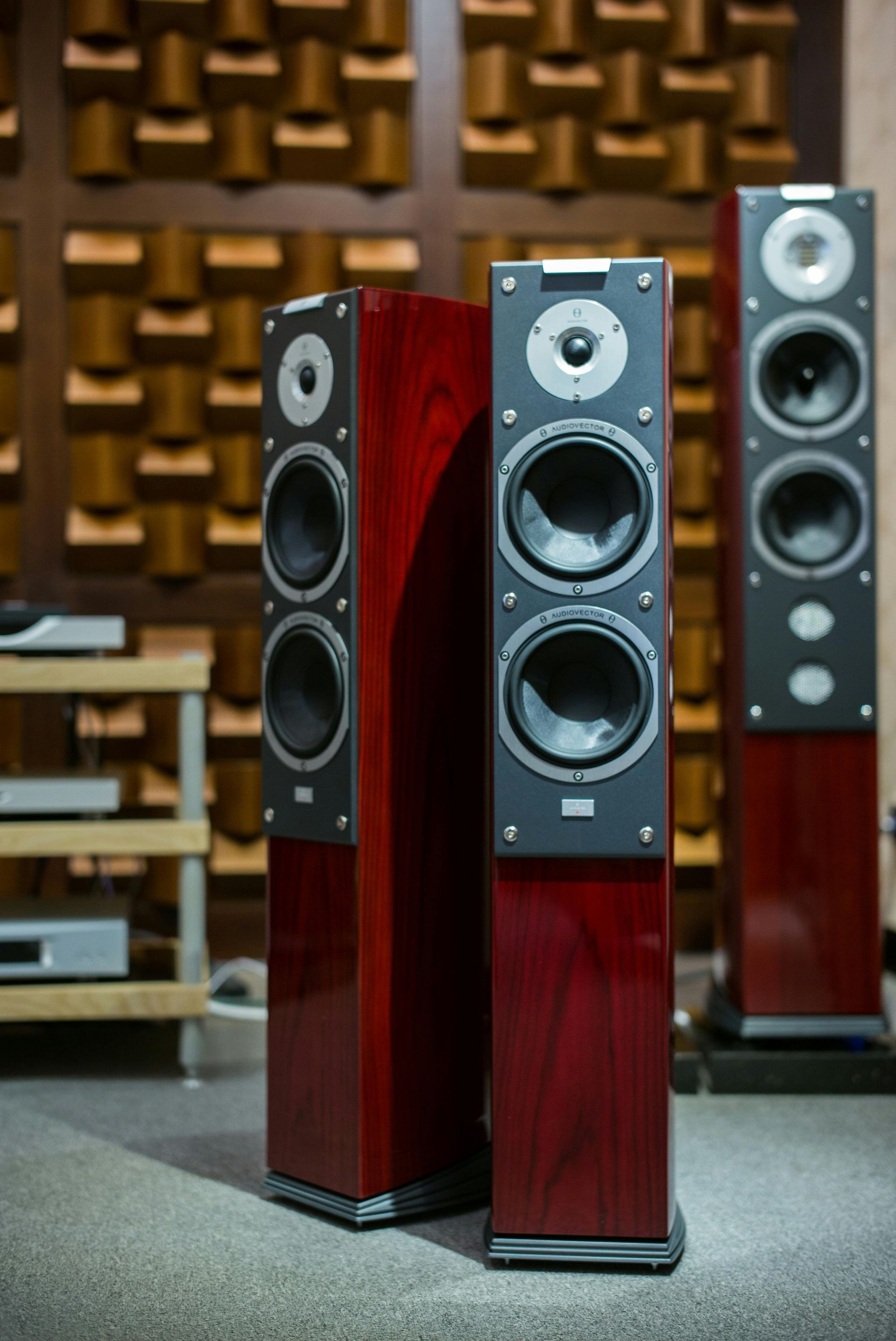 Three tall, red and black audio speakers on a gray floor in a sound-treated room.