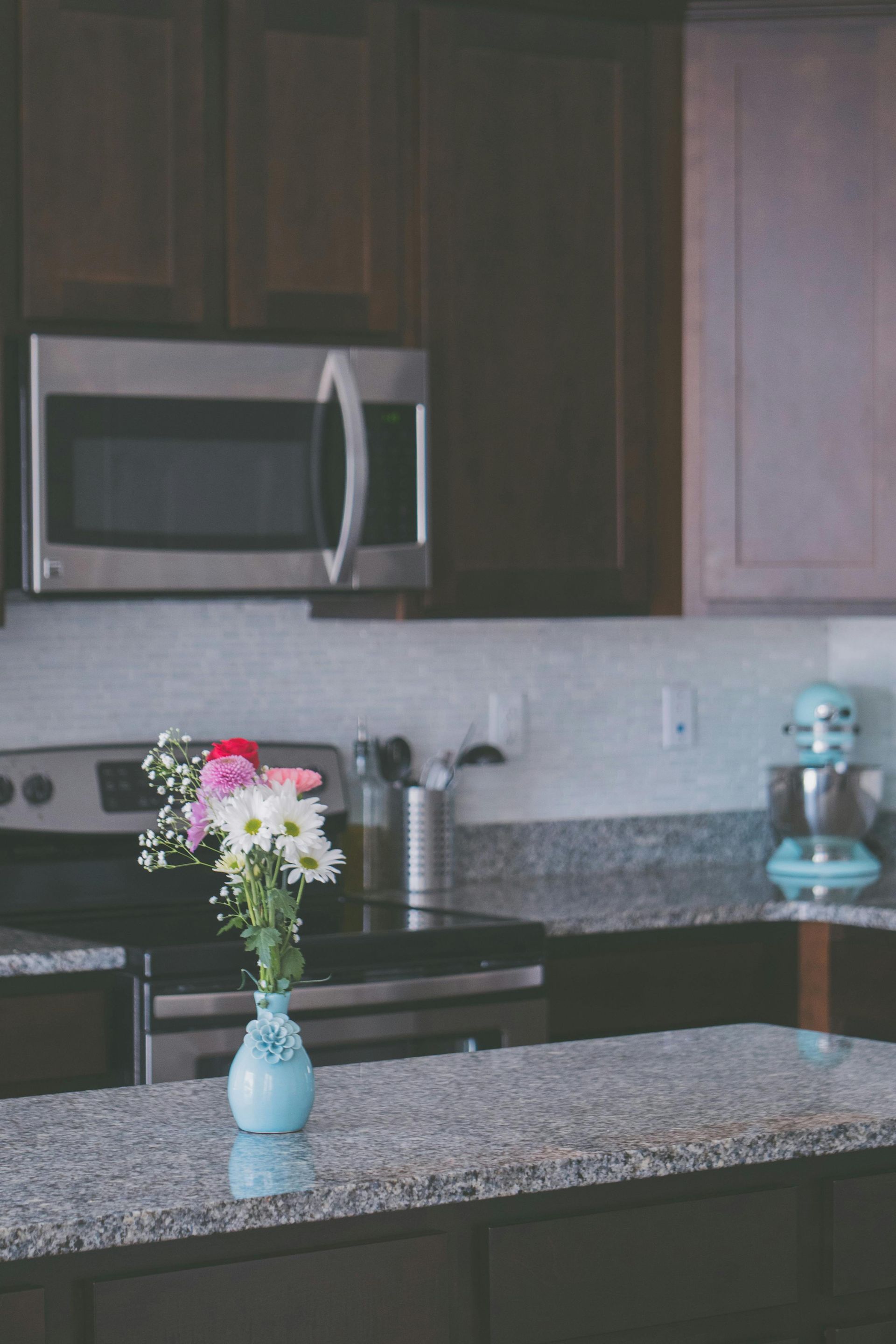 Kitchen with granite countertop, microwave, stove, flowers in blue vase, and turquoise mixer.