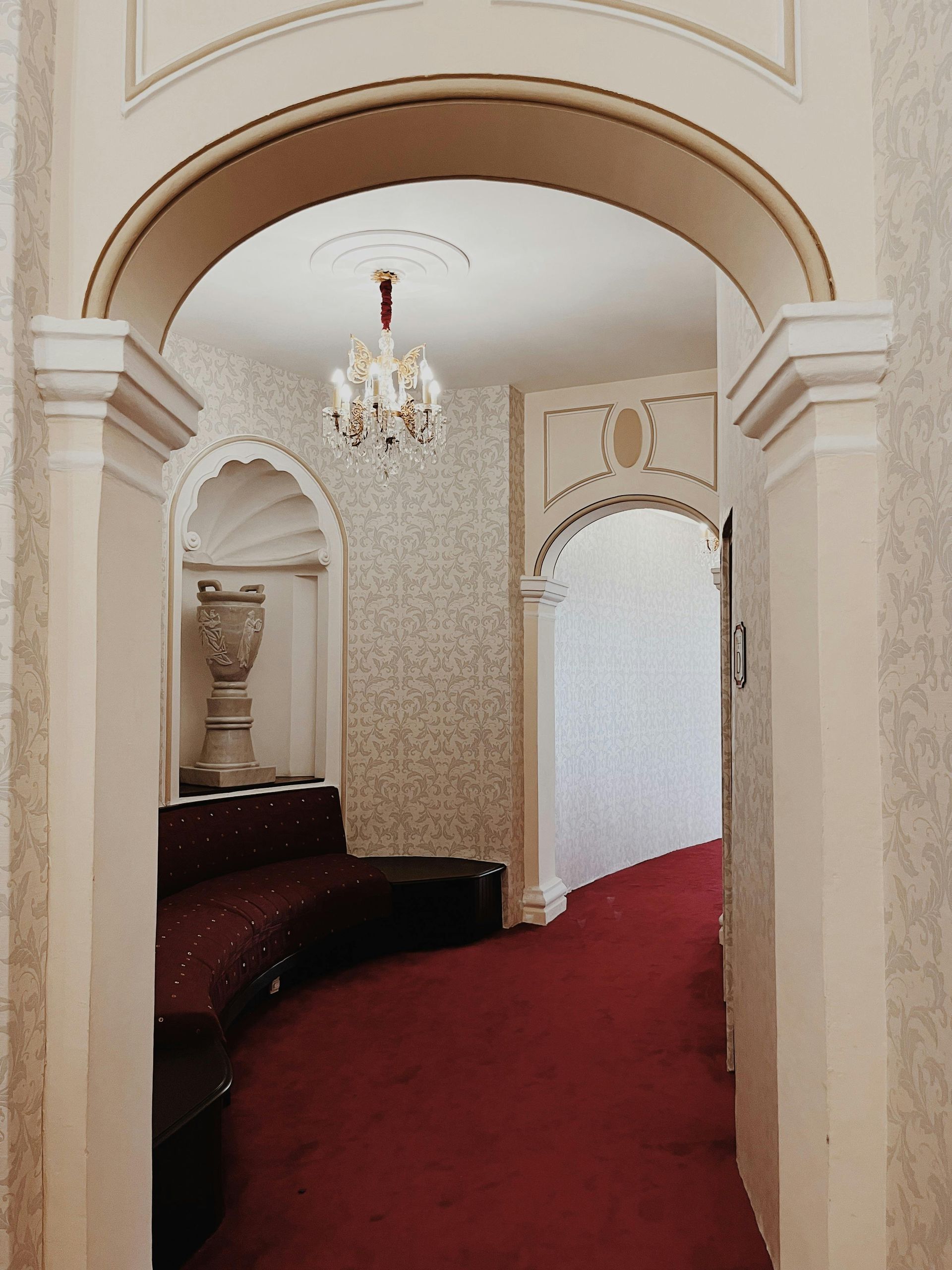 Arched doorway into a hallway with red carpet and a built-in sofa, ornate details.
