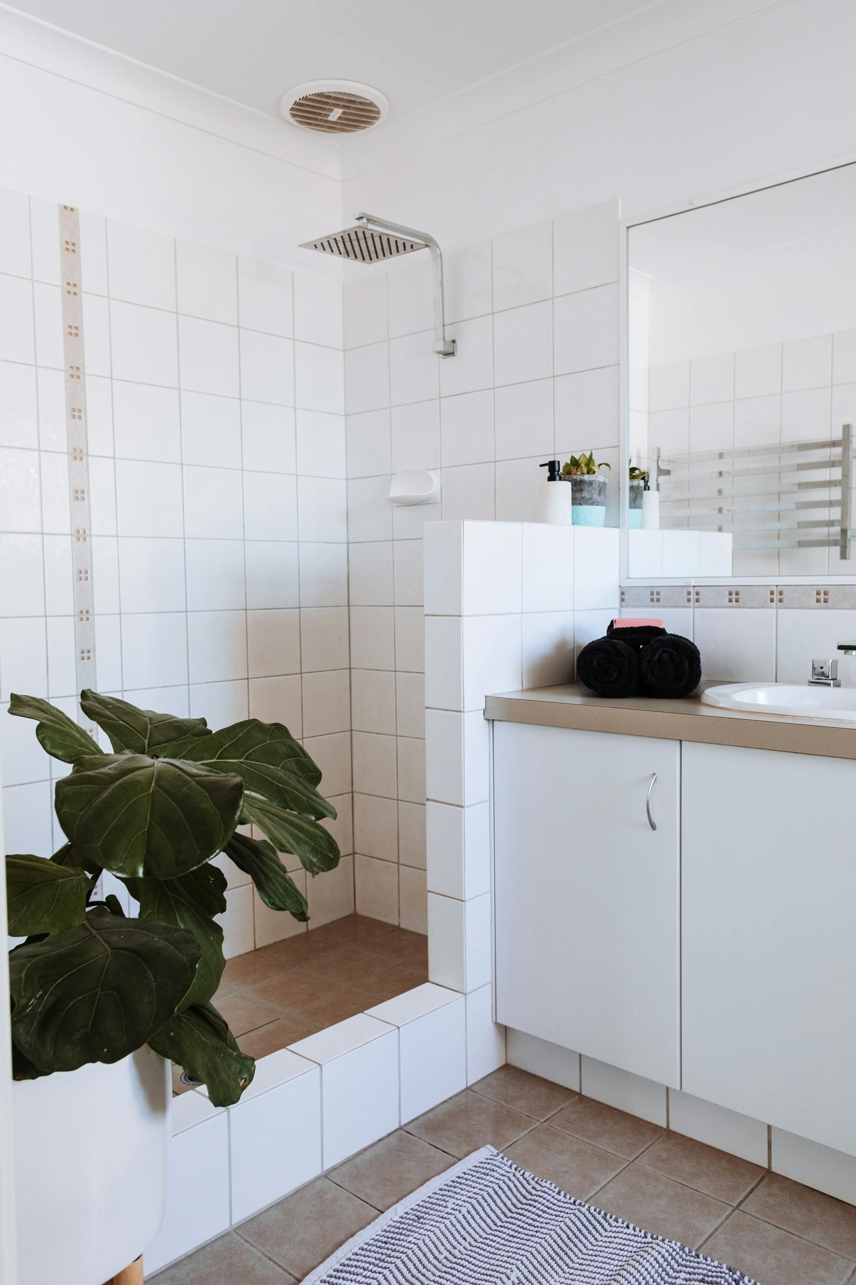 White tiled shower stall in a bright bathroom with a plant, countertop, and a mirror.