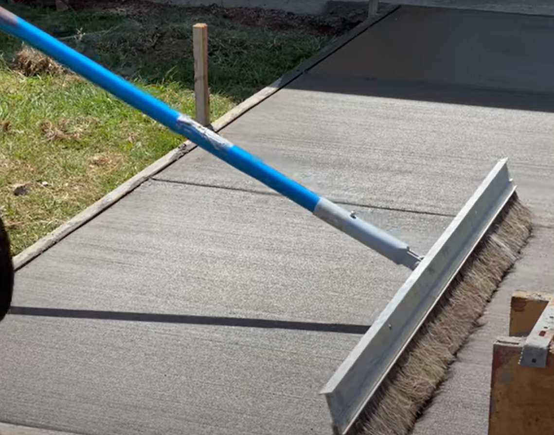 Concrete worker adding traction to a new concrete walkway with a broom finish