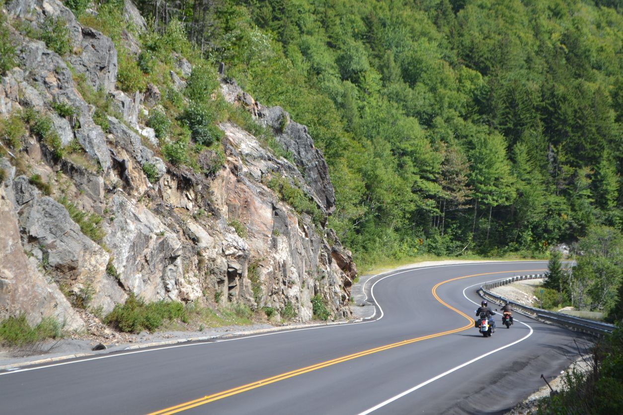 Picture is 2 motorcyclist riding down a mountain side road.