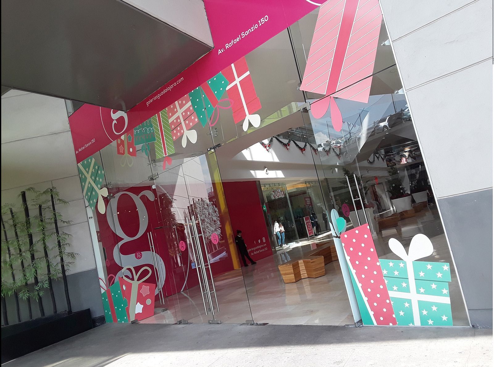 Escaparate decorado con cajas de regalo de color rosa y turquesa y una pancarta con temática navideña.