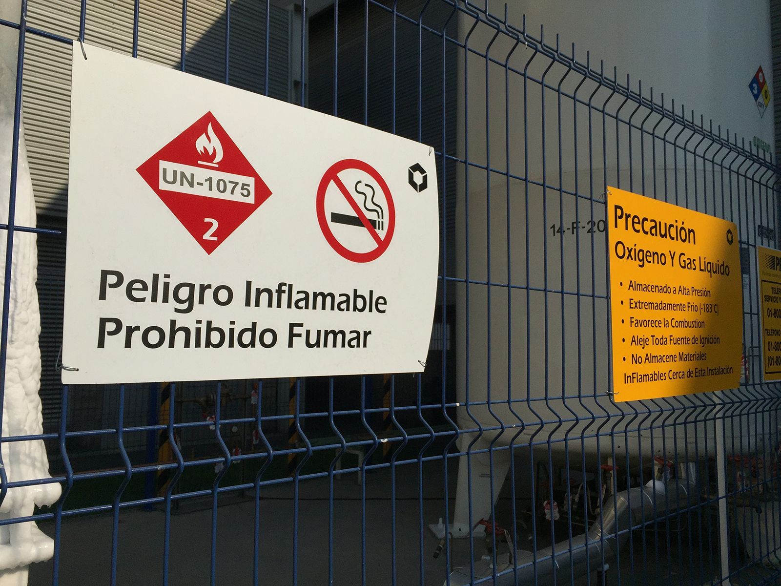Cartel advierte de material inflamable, prohibido fumar, al lado de un tanque.