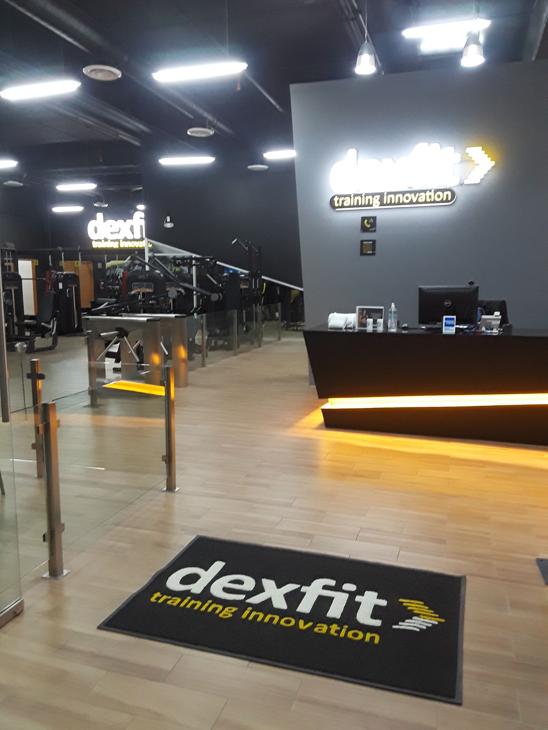 Entrada al gimnasio “dexfit training innovation” con mostrador de recepción y equipamiento fitness.