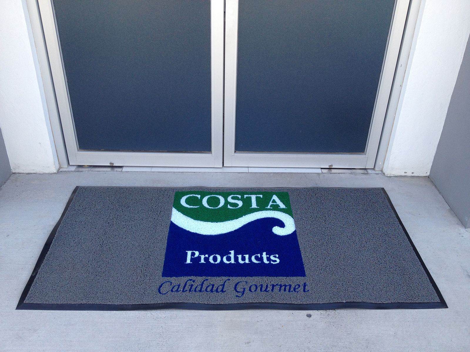 Puerta de entrada con felpudo con el logo de “Costa Products”.