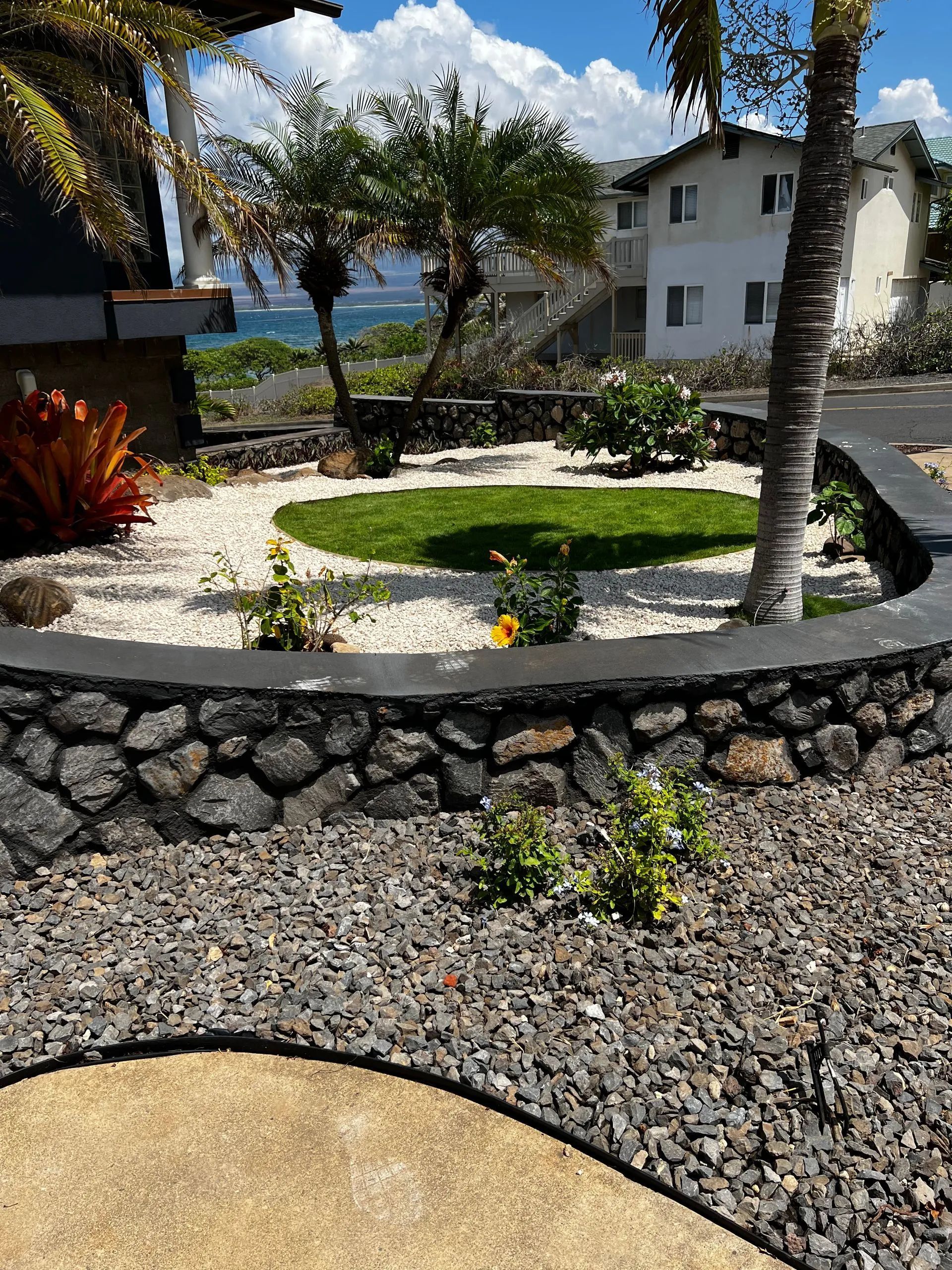 A stone wall surrounds a lush green garden with a house in the background.