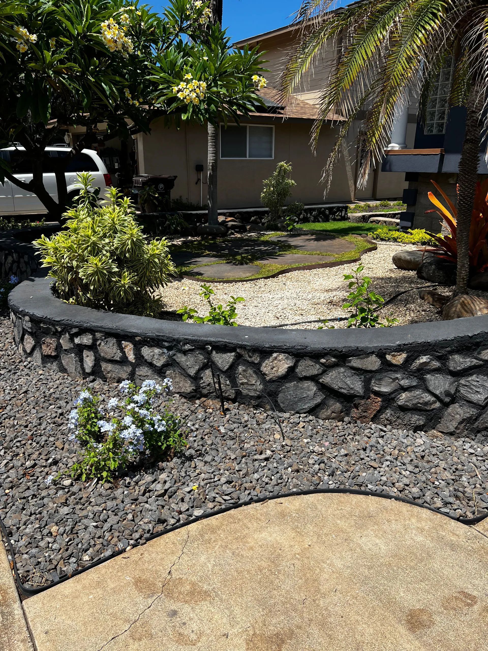 A stone wall surrounds a lush green garden in front of a house.