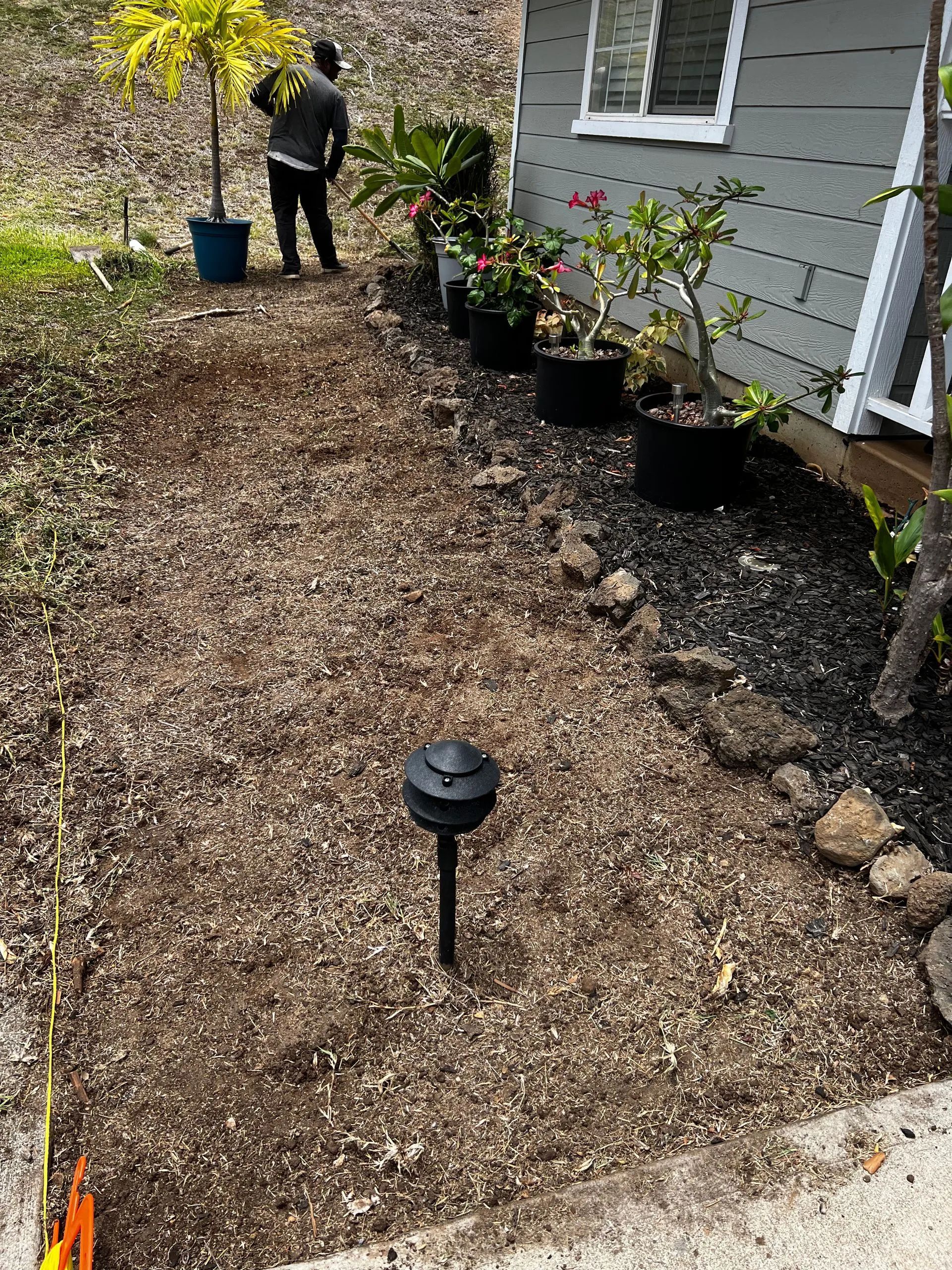A man is standing on a dirt path in front of a house.