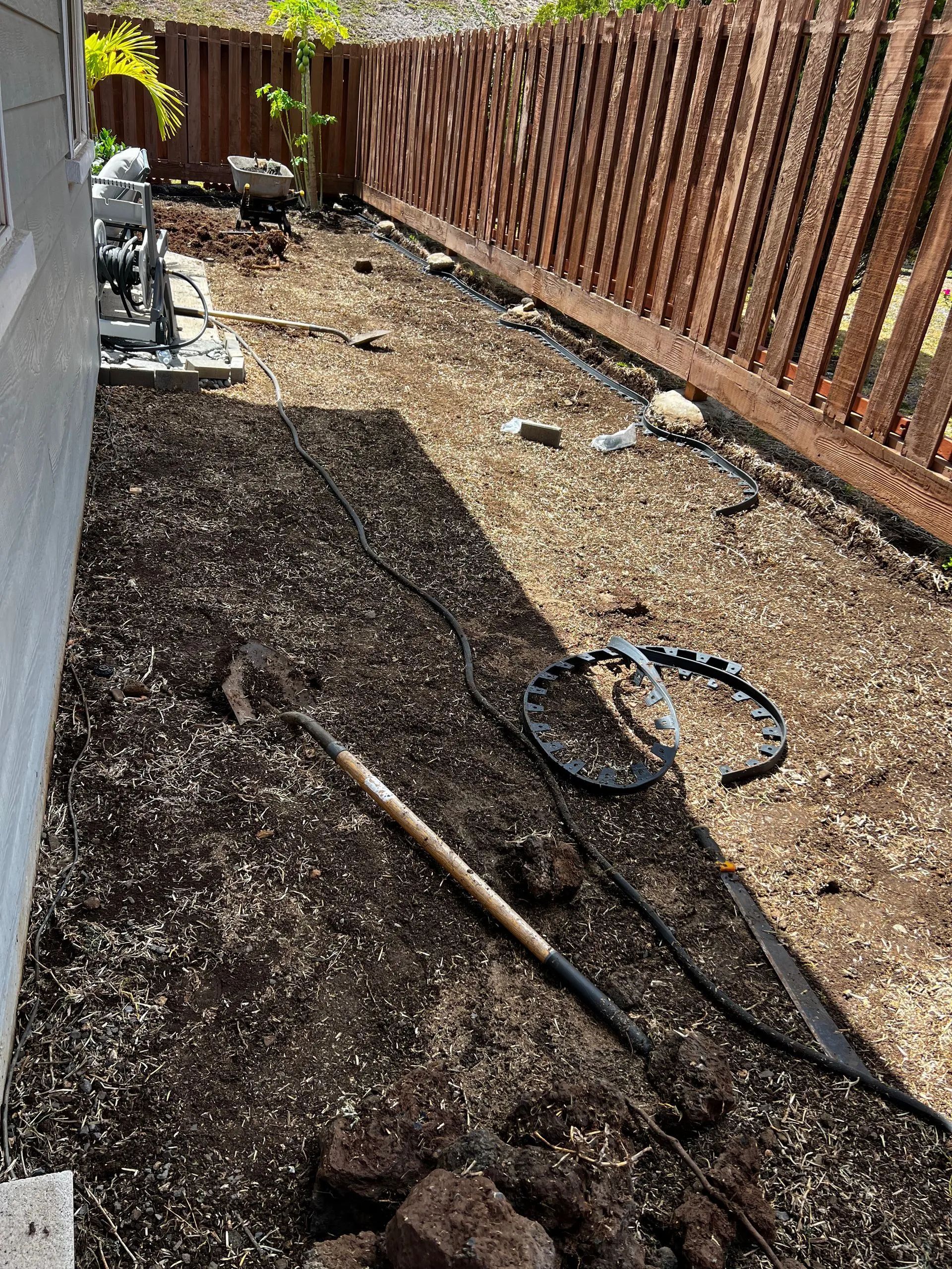 A backyard with a wooden fence and a pile of dirt and tools.
